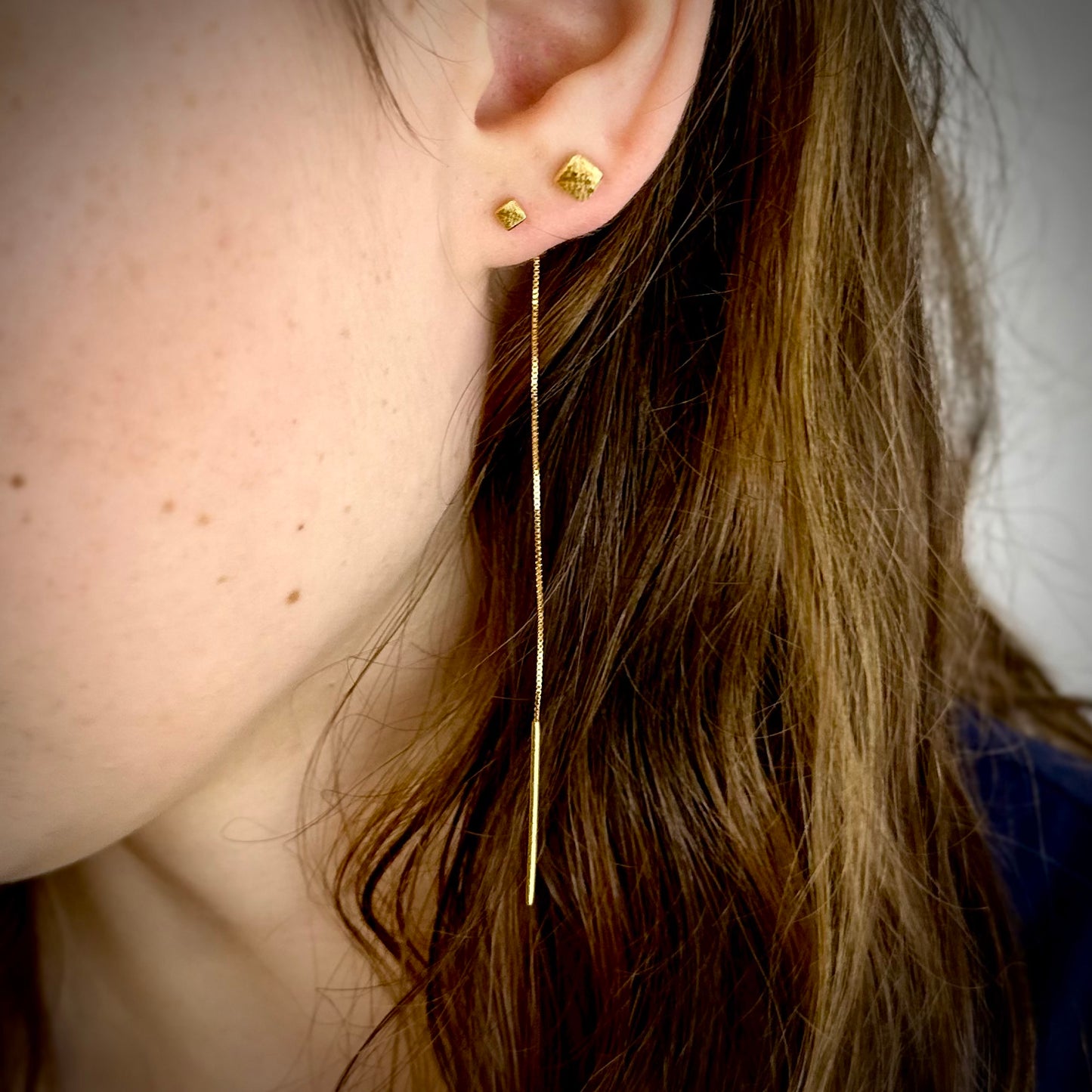 Close-up of a person wearing gold threader earring and a cube stud with a blurred background