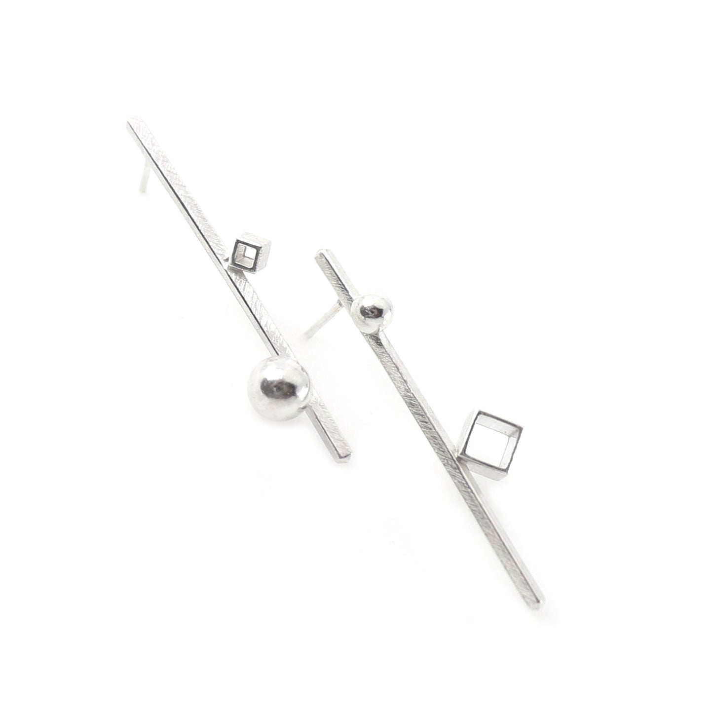 A pair of minimalist silver geometric long bar earrings with textured polished spheres, and cube elements, displayed on a clean white background.