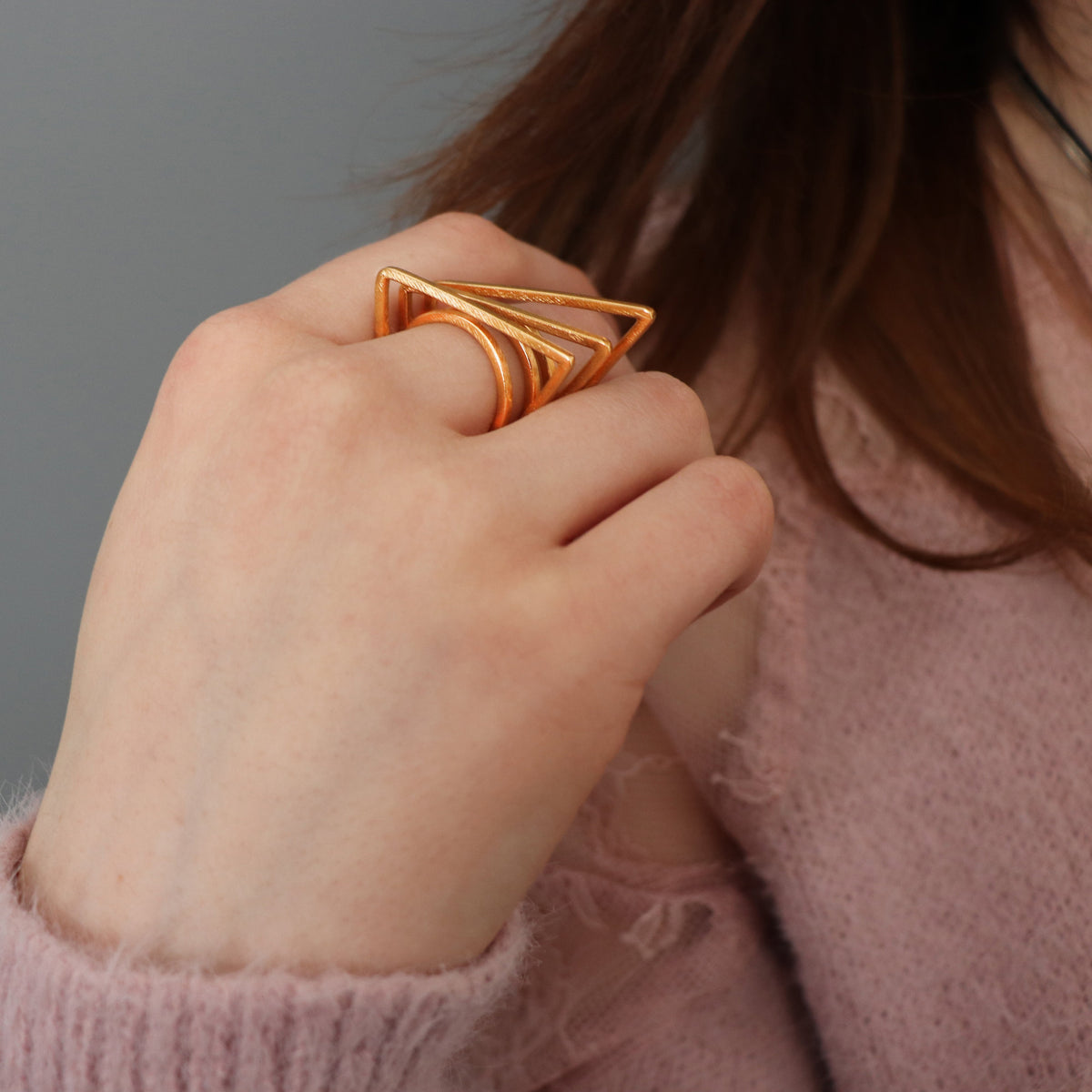 Hand wearing a geometric gold ring against a neutral background