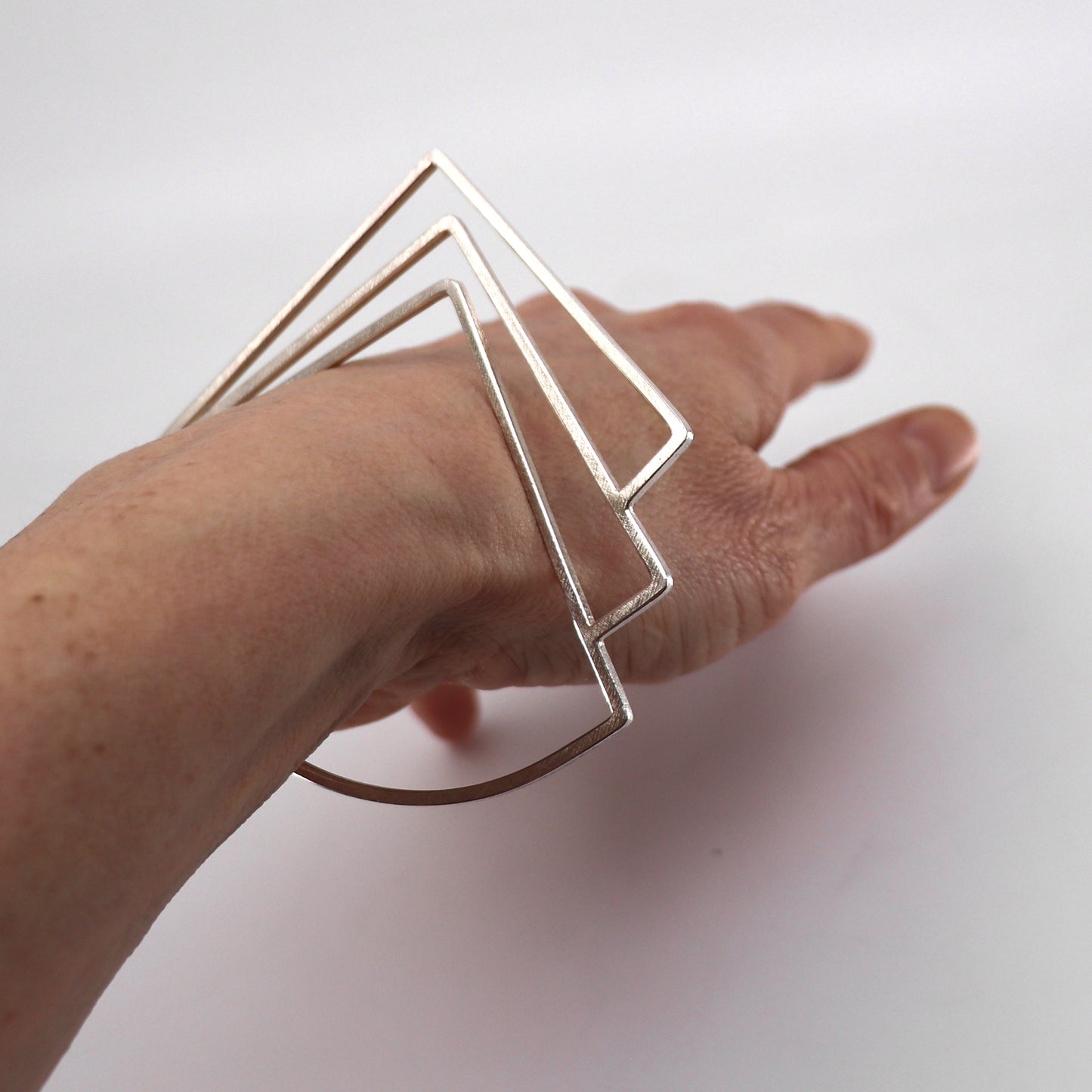 Hand wearing a silver geometric bracelet on a white background
