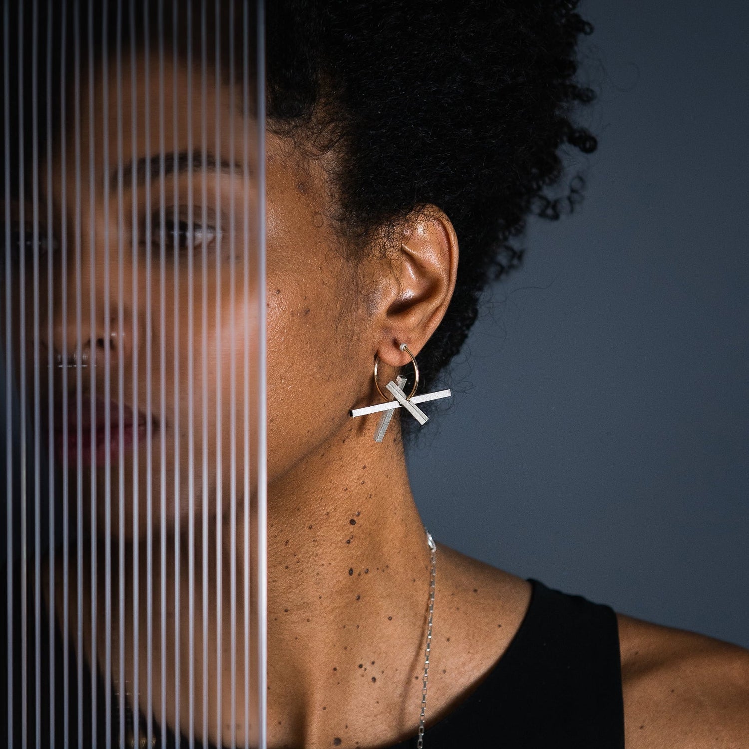 A close-up lifestyle shot of a model wearing a silver and gold geometric brutalist inspired earring against a dark gray background.