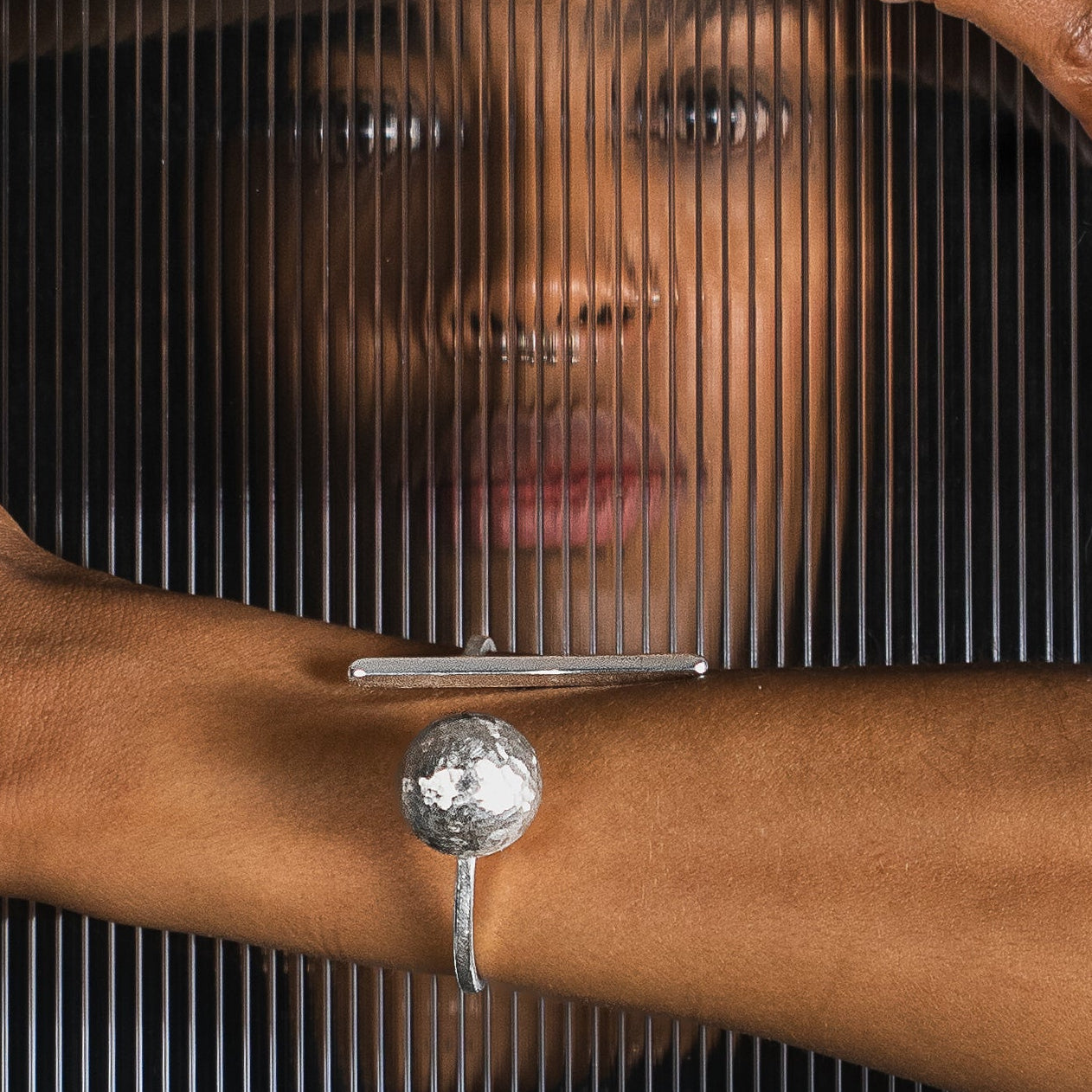 A close-up lifestyle shot of a model wearing a architectural silver bar cuff with a ball element. 