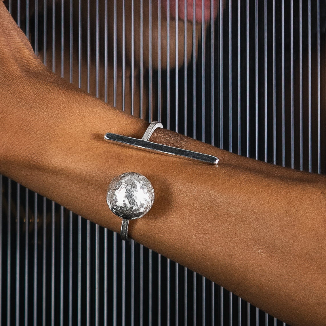 A close-up lifestyle shot of a model showcasing a silver geometric cuff bangle with T-bar and a ball  element.