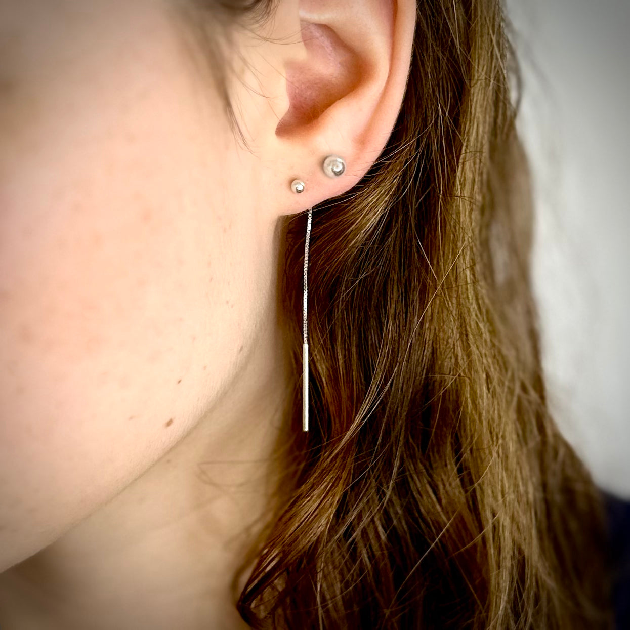 Close-up of an ear with silver earlace threader earrings on a neutral background