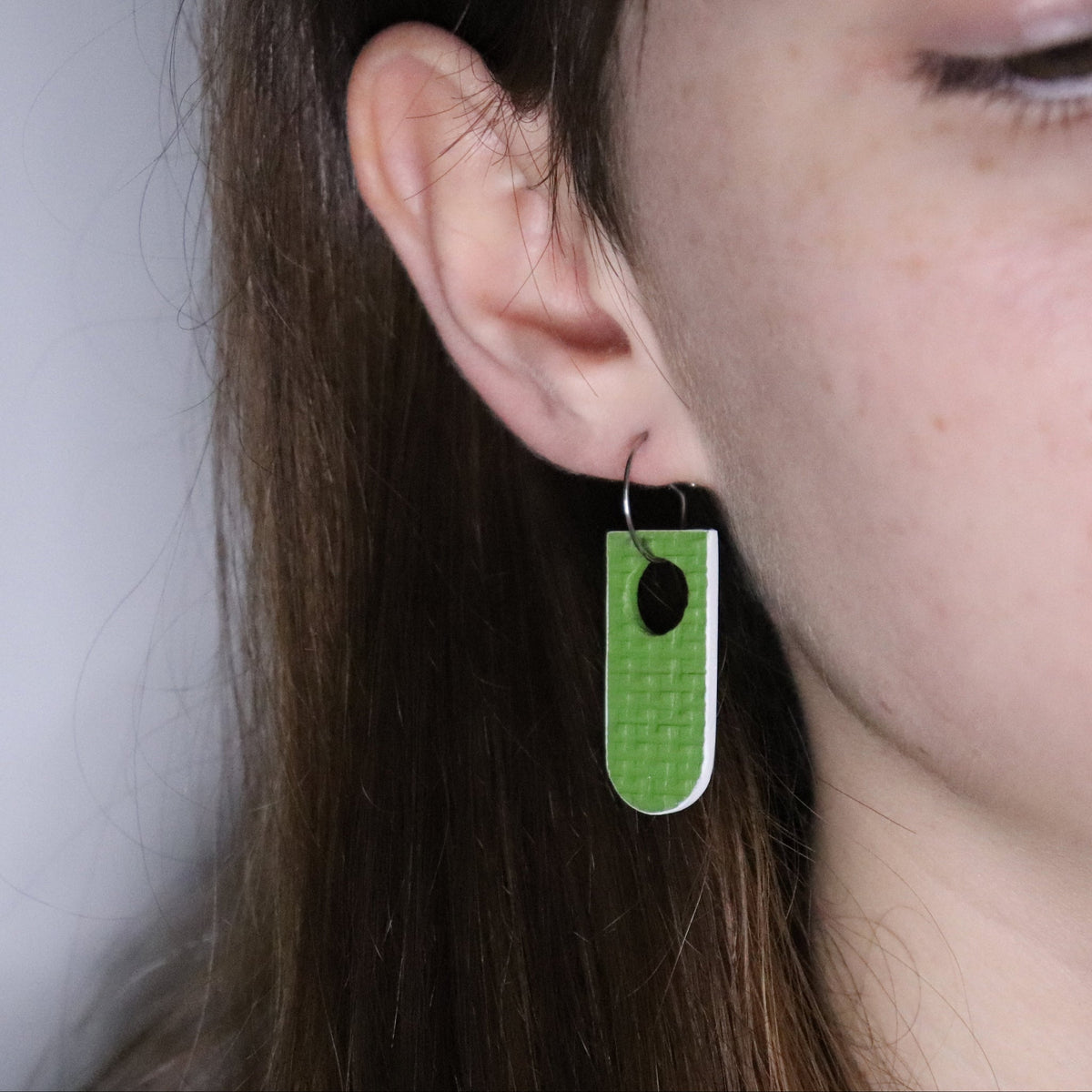 Close-up of a person wearing a green and white earring against a neutral background