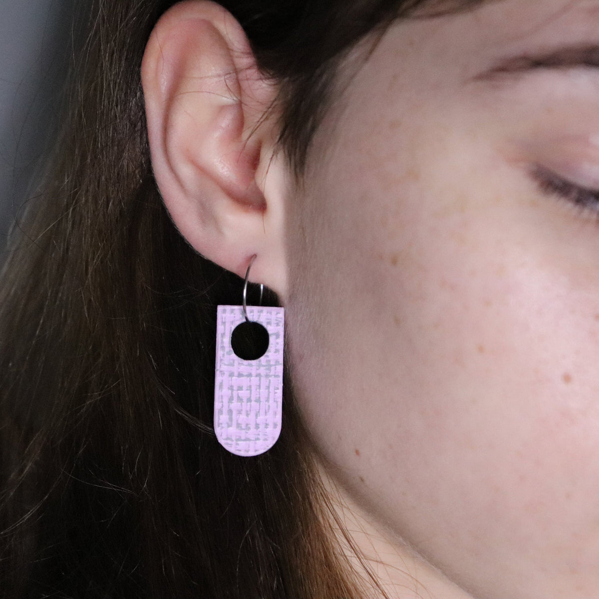 Close-up of a person wearing a pink textured earring hanging on a small steel hoop with a hole center.