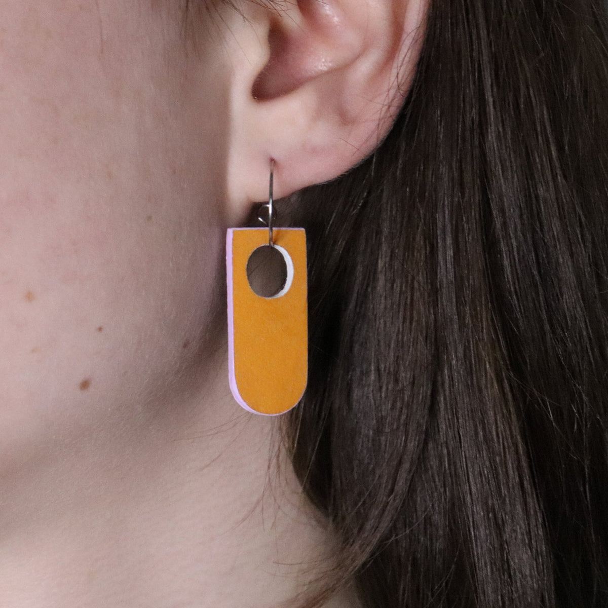 Close-up of a person wearing a orange and lilac earring made from recycled linoleum