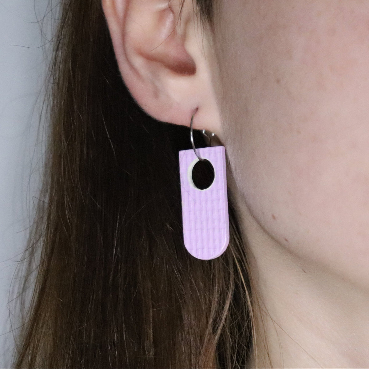 Close-up of a person wearing a lilac earring made of recycled linoleum.