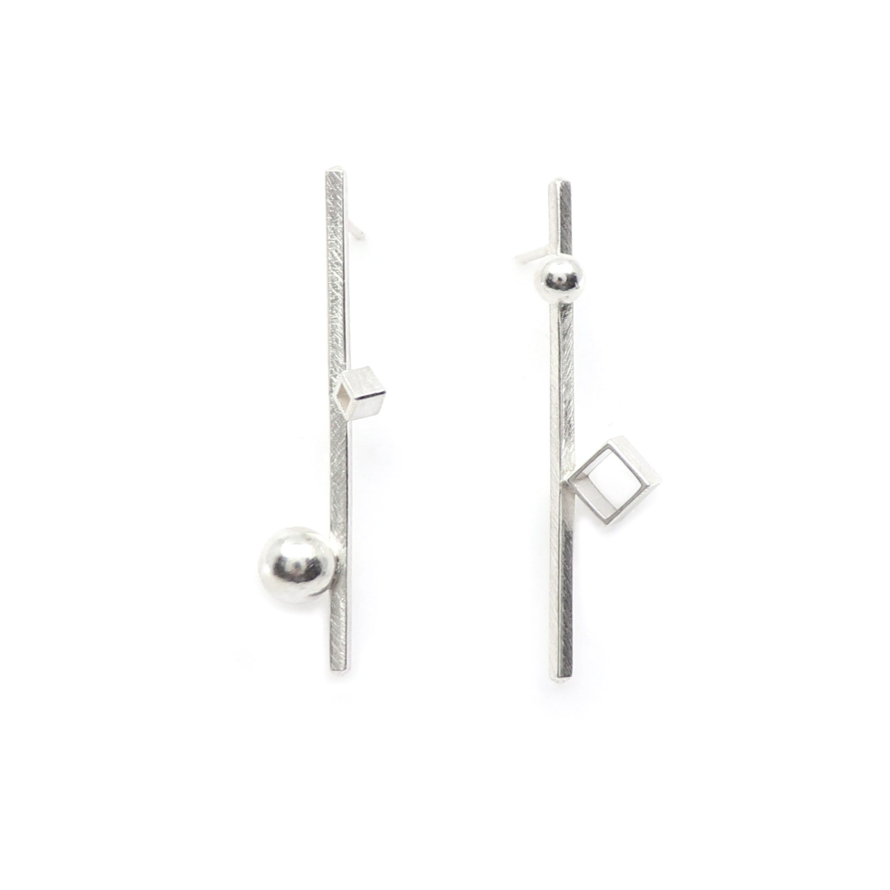 A pair of architectural sterling silver geometric earrings on a clean white background. One earring features a vertical textured bar with a spherical bead at the bottom and a small square at the top, while the other features a similar vertical bar with a square at the top and a larger square at the bottom.