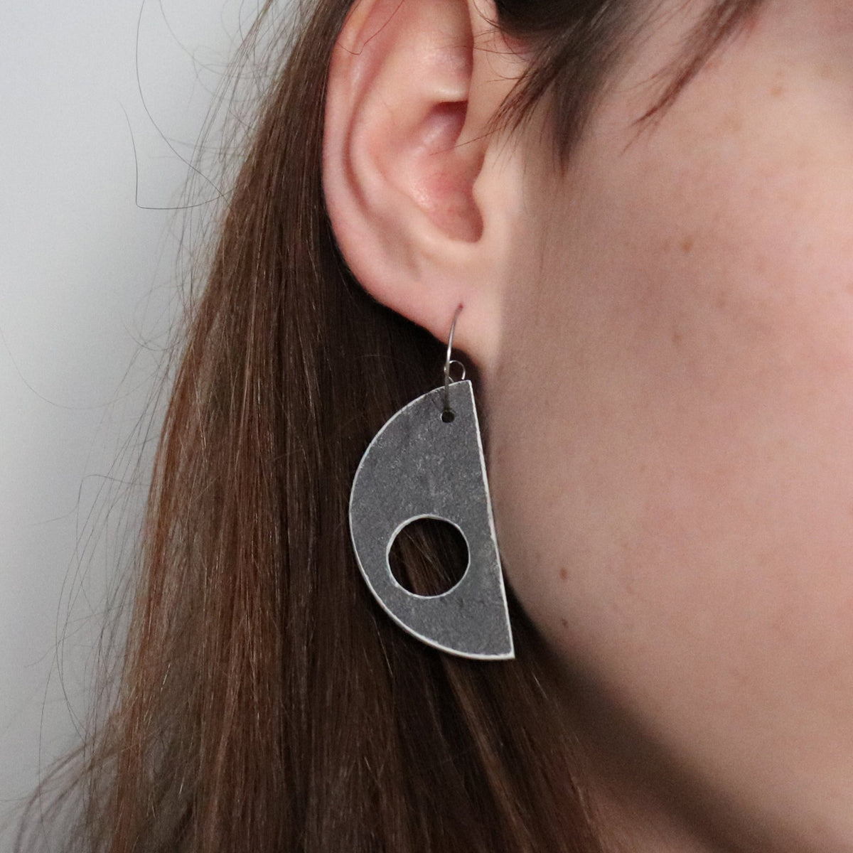 Close-up of a person wearing a grey geometric earring against a neutral background