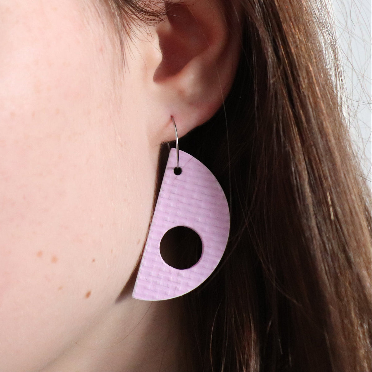 Close-up of a person wearing a lilac earring with a circular cutout