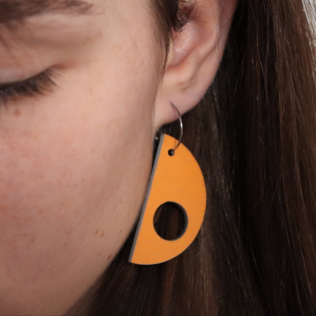 Close-up of a person wearing an orange teardrop-shaped earring.