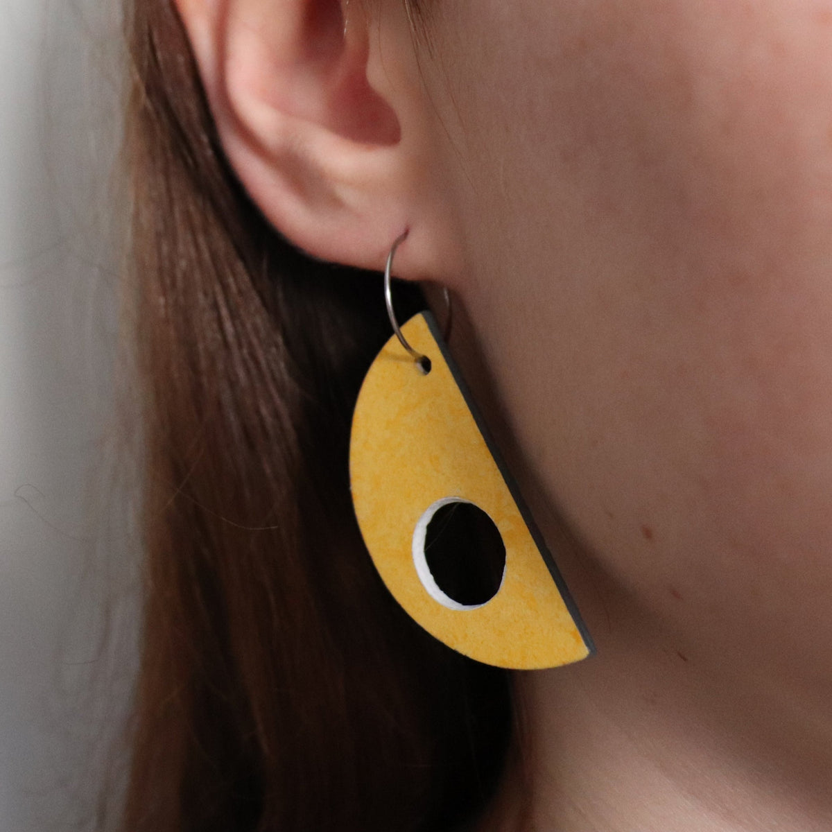 Yellow half-circle earring with a black center worn by a person.