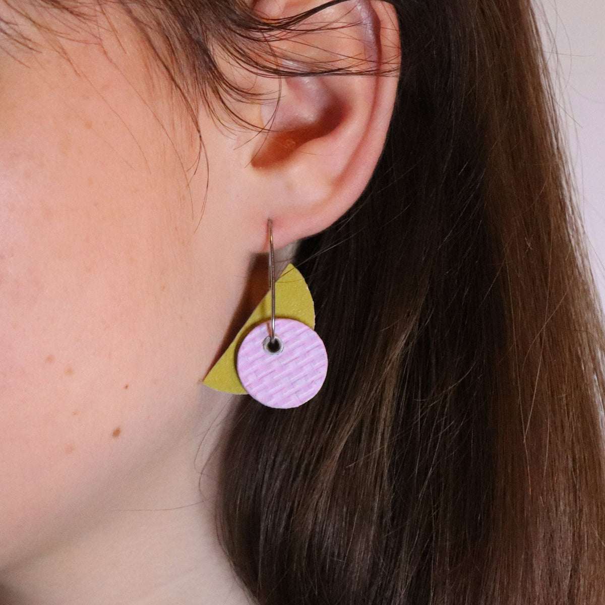 Close-up of a person wearing a colorful earring with a pink circle and yellow triangle.