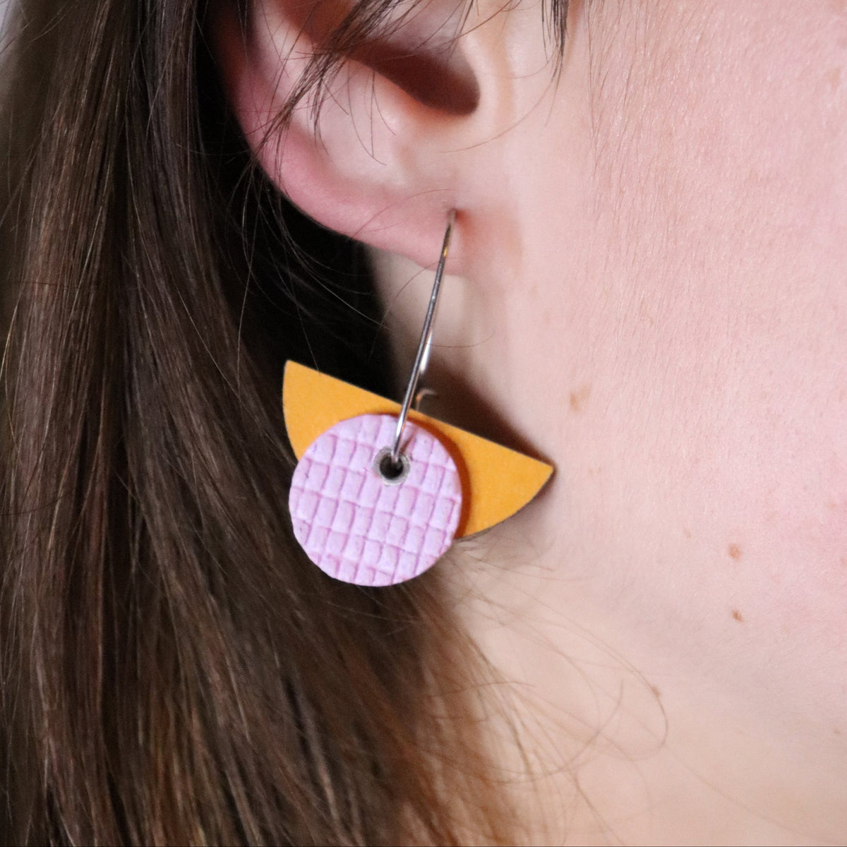 Close-up of a person wearing a colorful earring with a pink and yellow design.