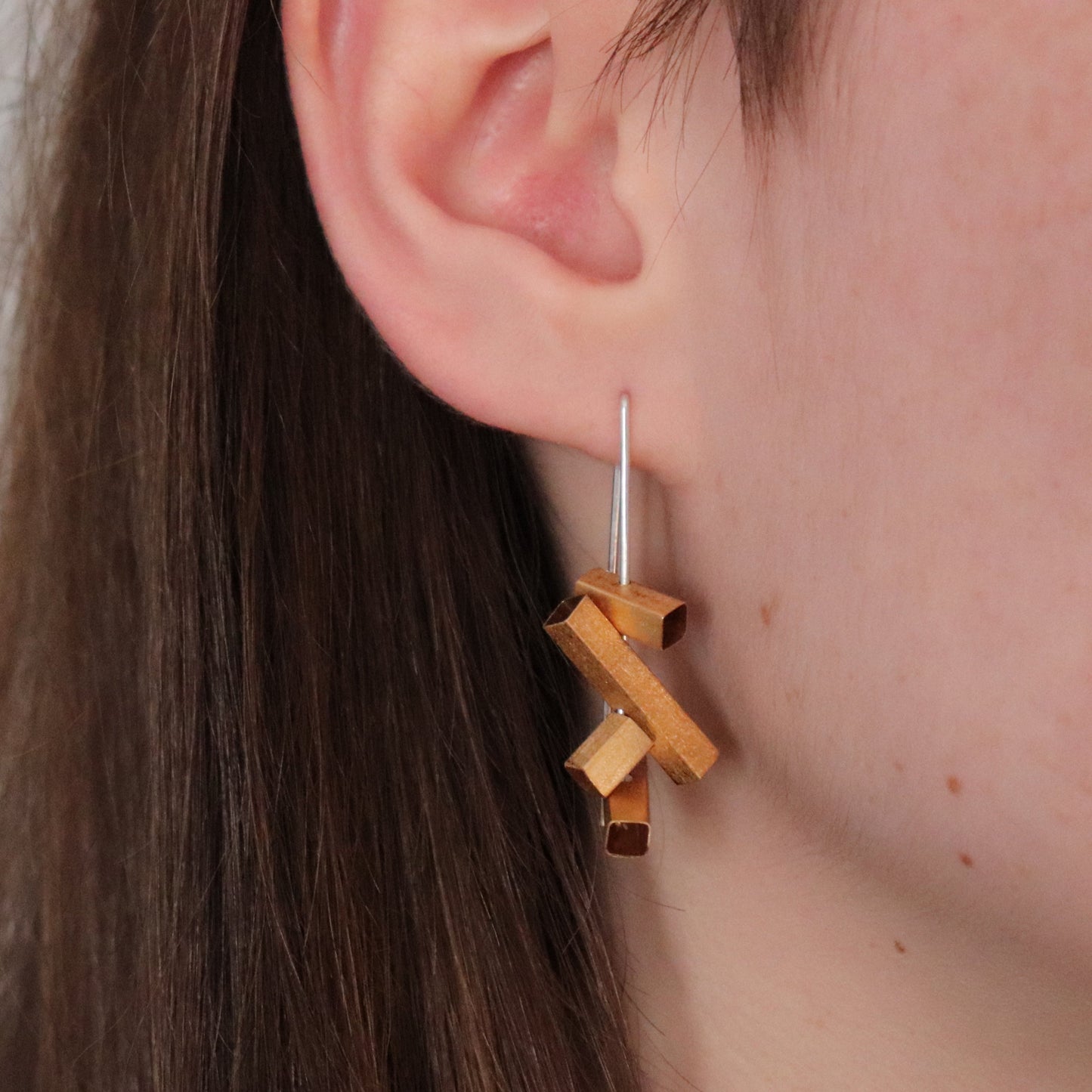 gold rectangles on silver wire earrings on an ear with a neutral background