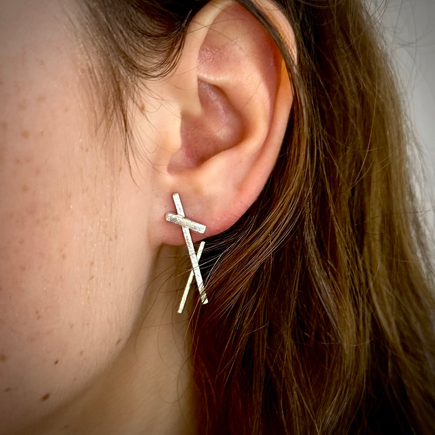 Close-up of an ear wearing a silver earring with a blurred background