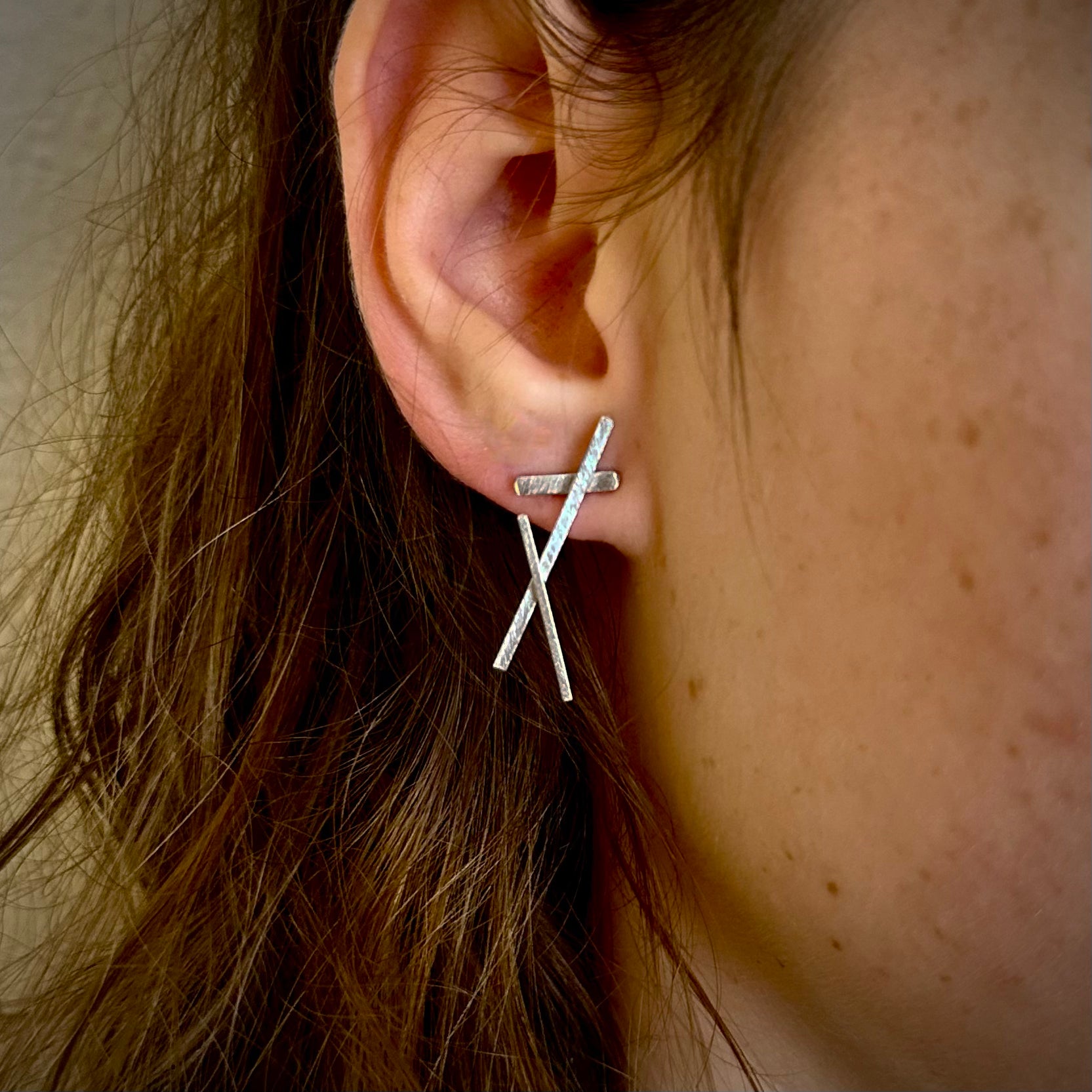 Silver cross-shaped earring worn by a person with brown hair.