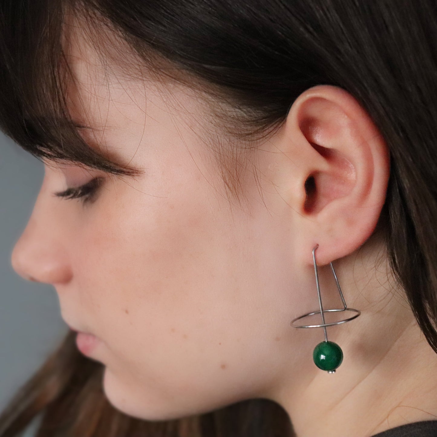Close-up of a person wearing a green agate geometric earring with a grey background