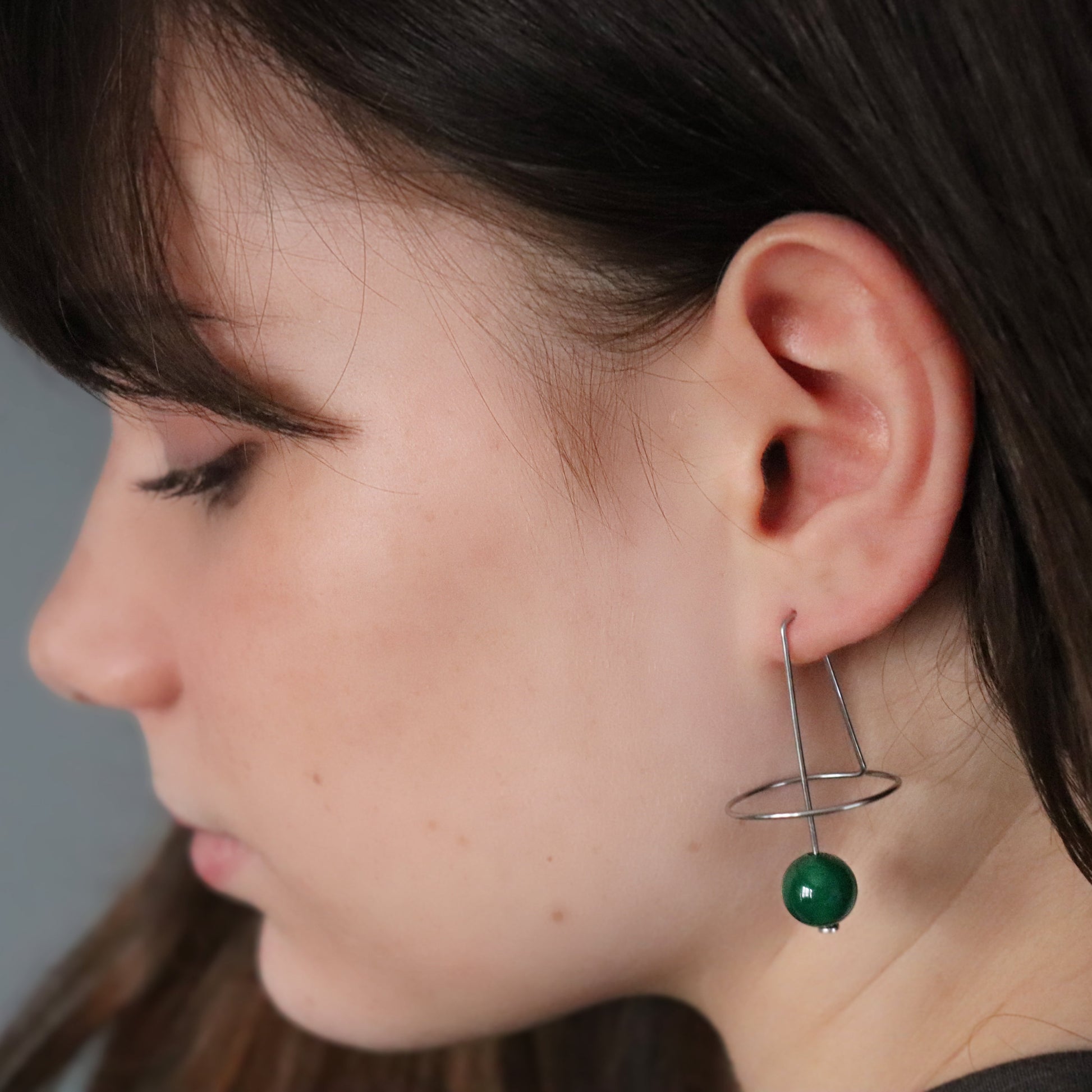 Close-up of a person wearing a green agate geometric earring with a grey background