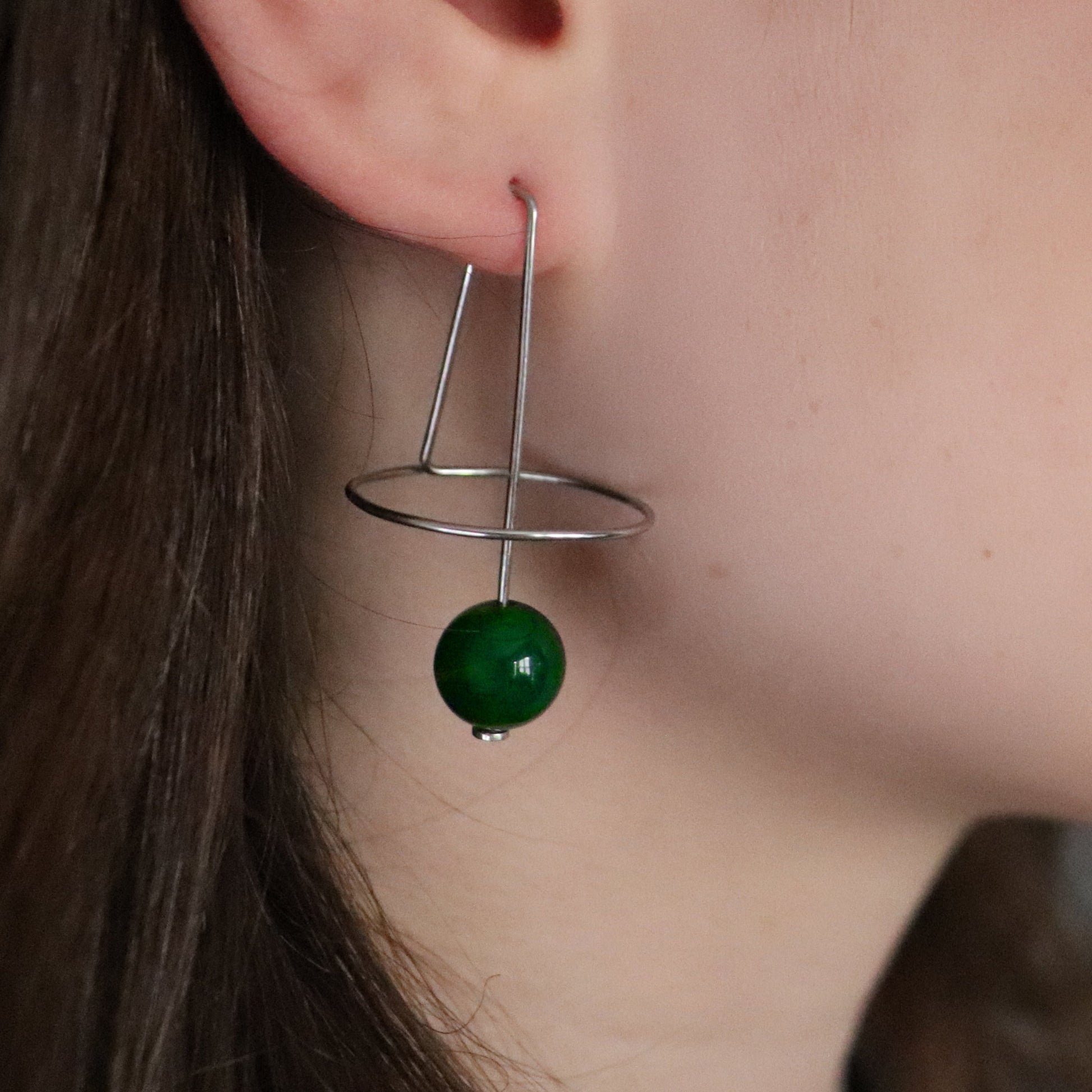 Geometric earring with a green agate bead worn by a person.