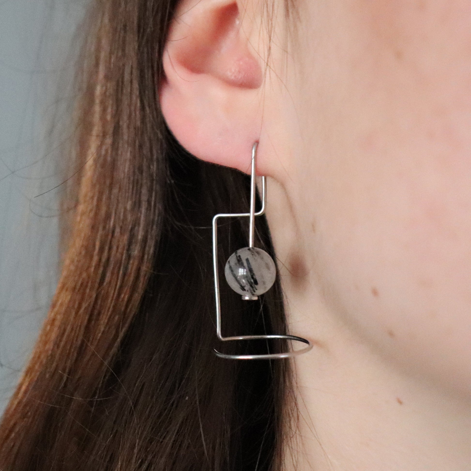 Close-up of a person wearing a geometric earring with a round rutilated quartz bead.