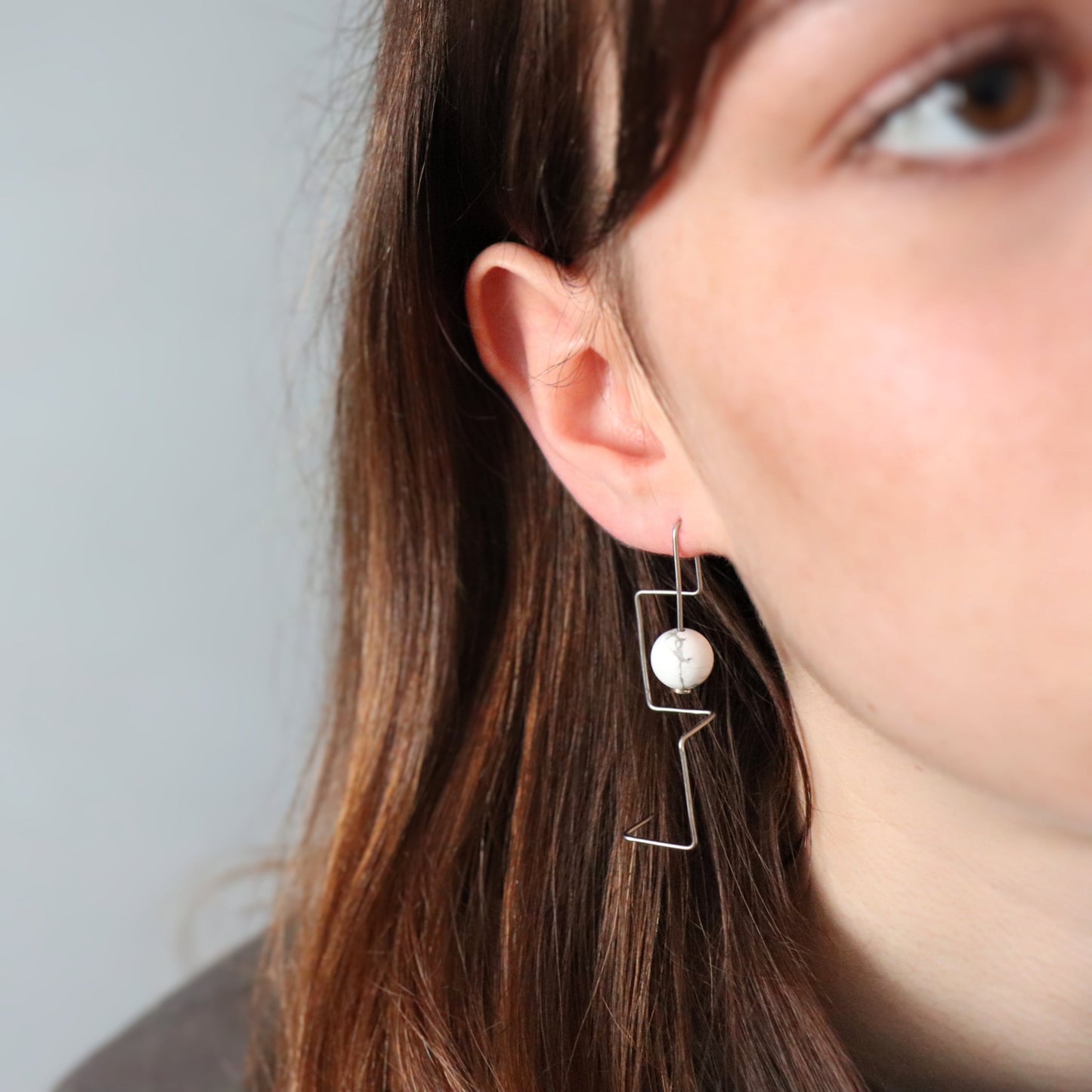 Close-up of a person wearing a unique earring with a howlite bead.