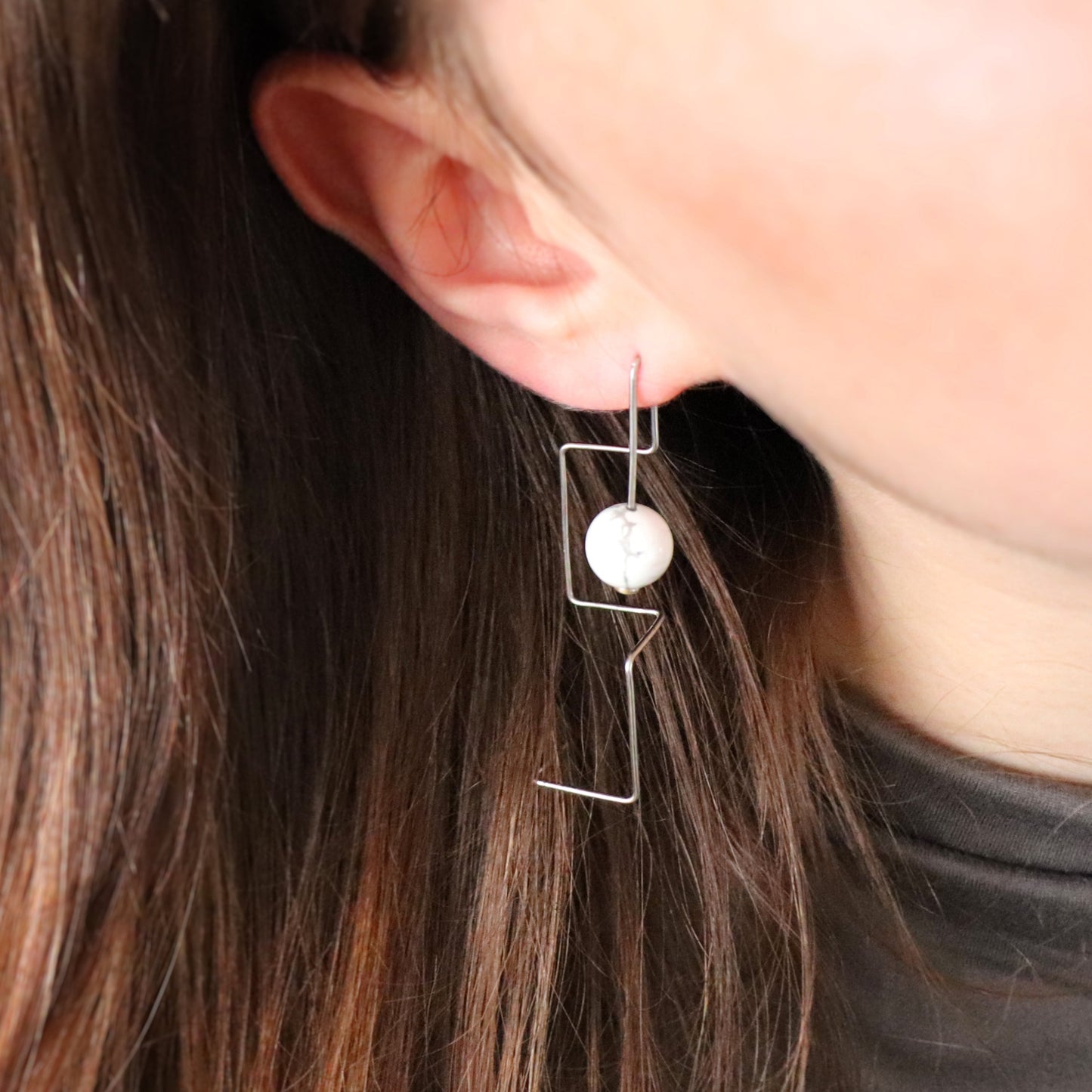 Close-up of an ear wearing a unique wire earring with a howlite bead.