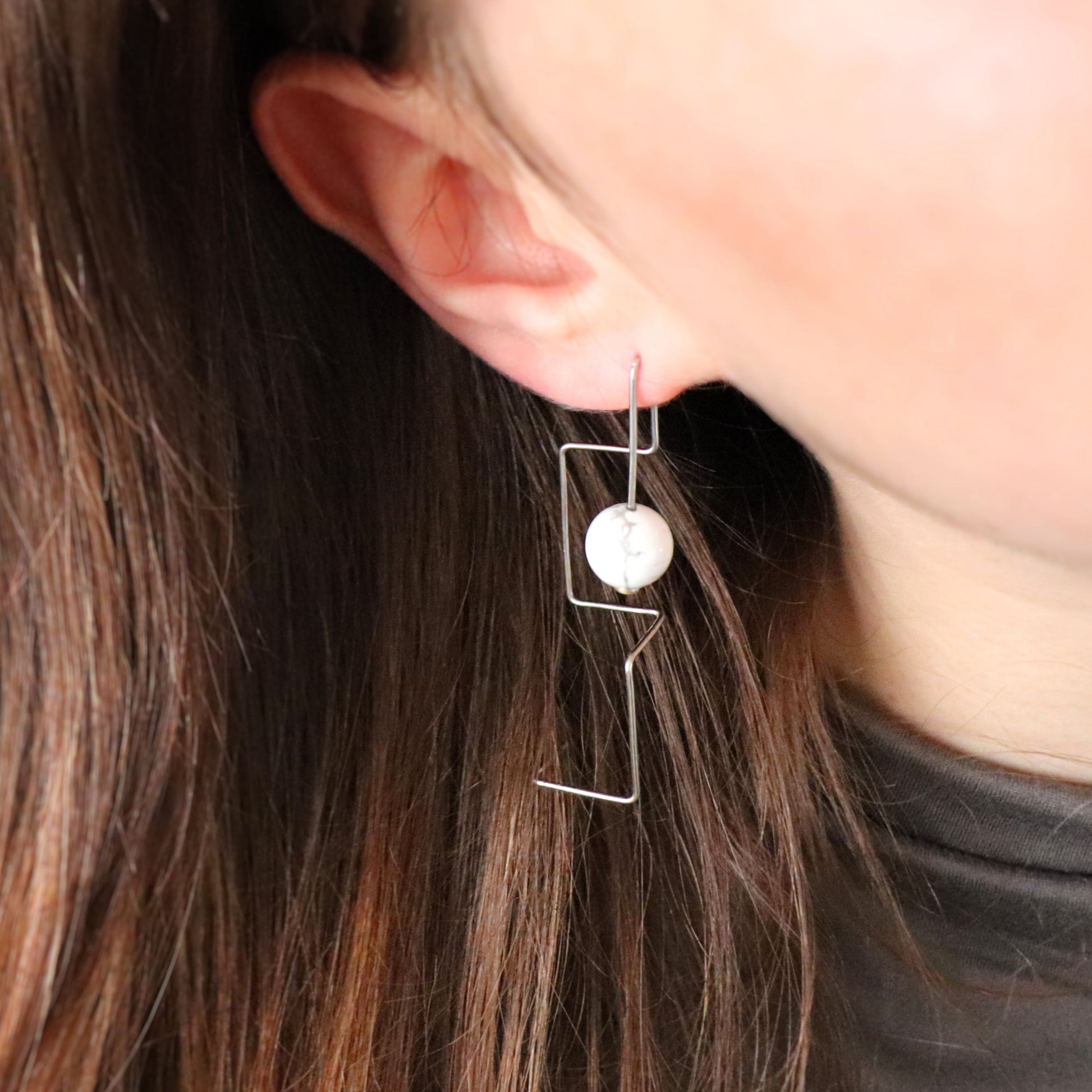 Close-up of an ear wearing a unique wire earring with a howlite bead.