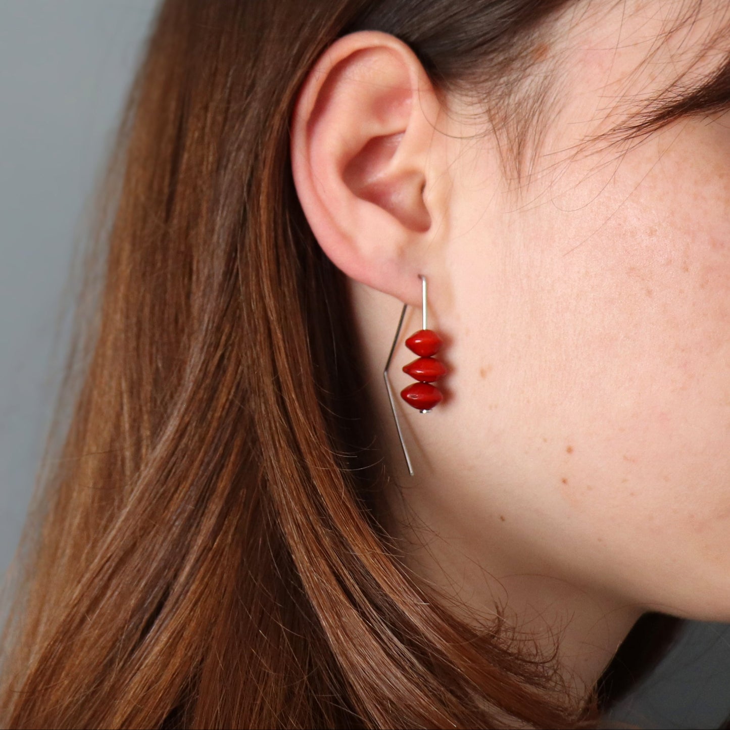 Close-up of a person wearing red beaded earrings with a neutral background