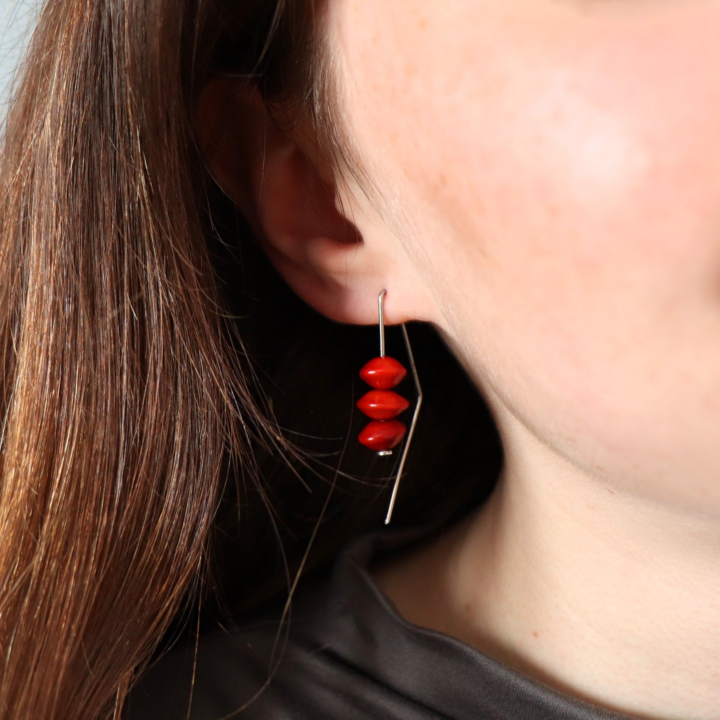 Close-up of a person wearing a red beaded earring with a blurred background
