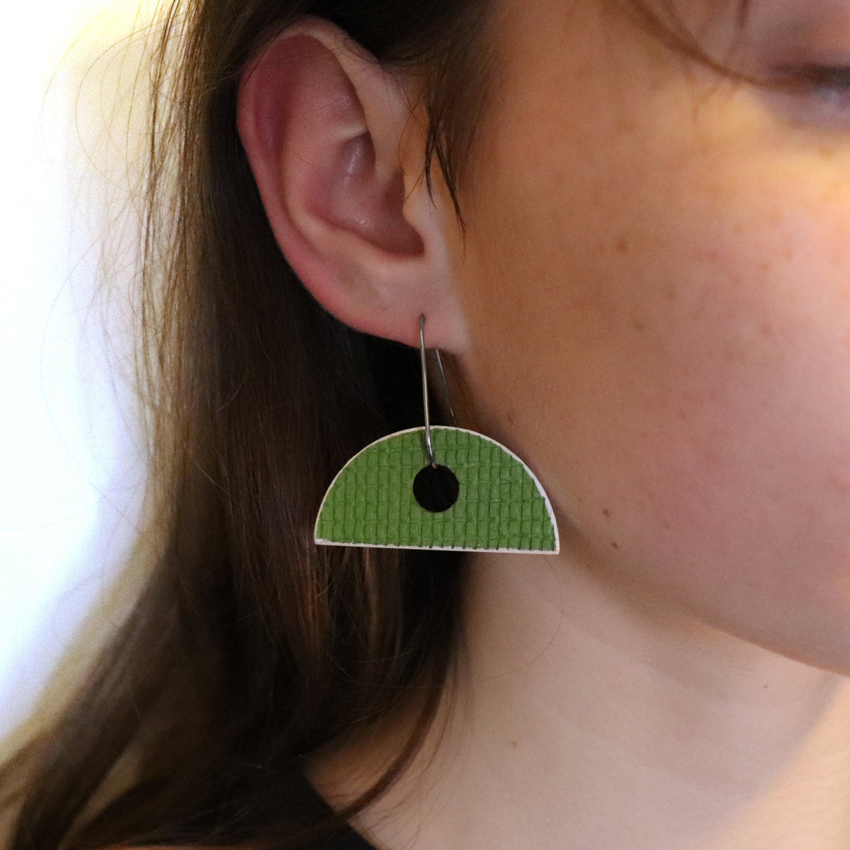 Green half-circle earrings worn by a person with a neutral background