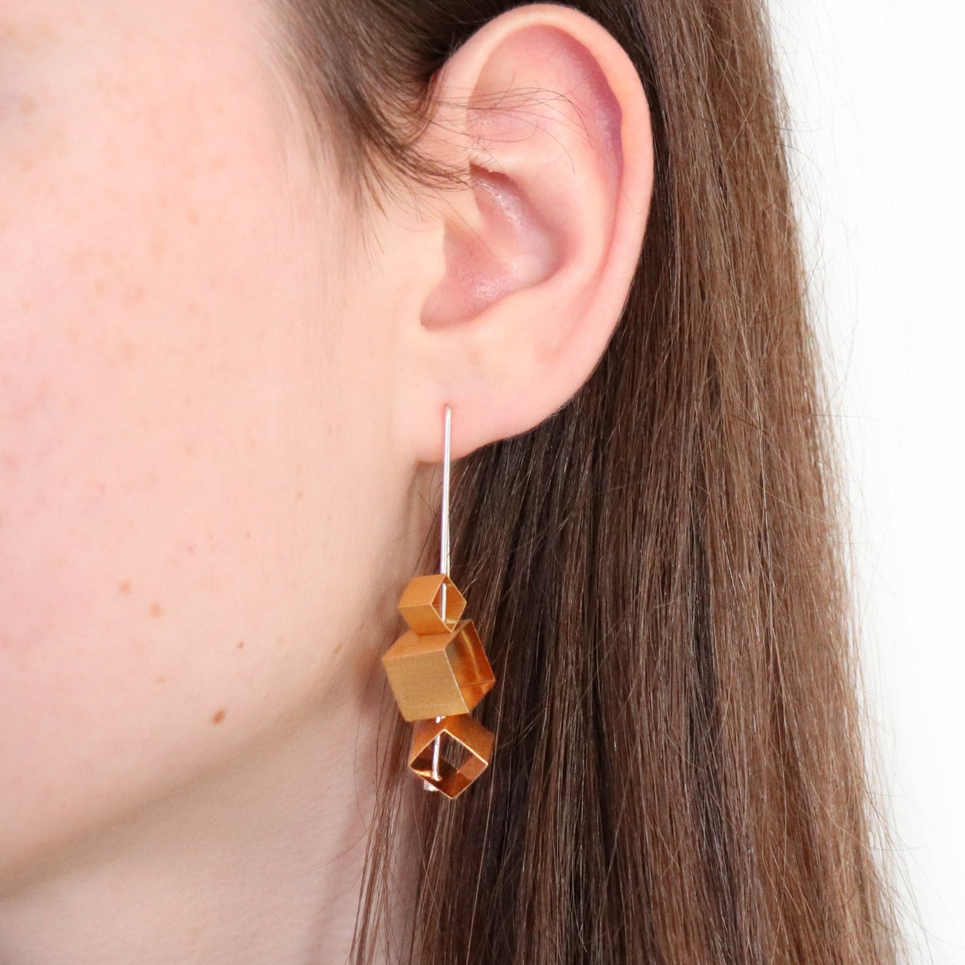 Close-up of an gold geometric earring worn by a person with brown hair.