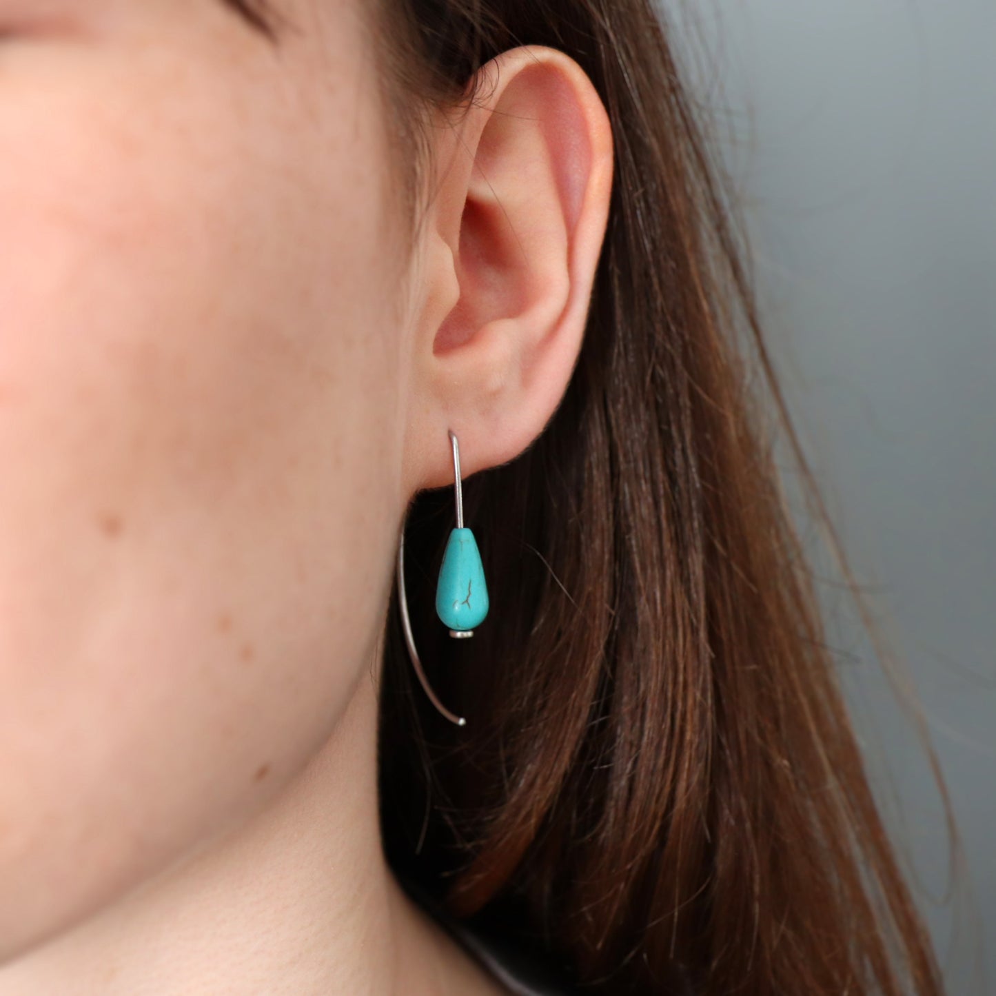 Close-up of a turquoise earring worn by a person with a neutral background
