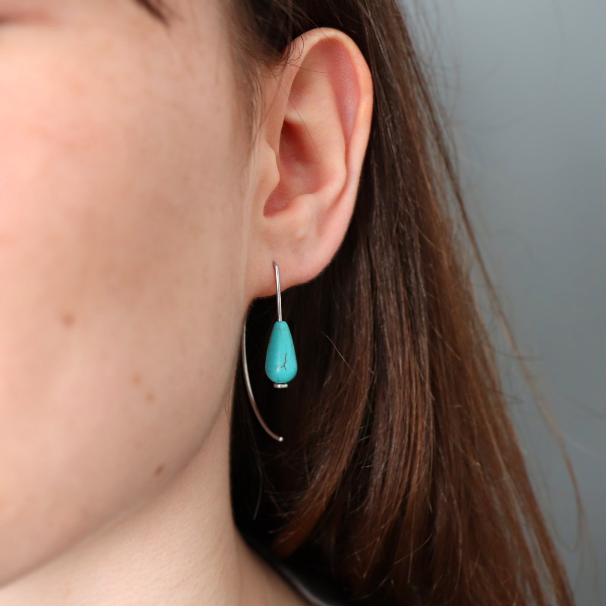 Close-up of a turquoise earring worn by a person with a neutral background