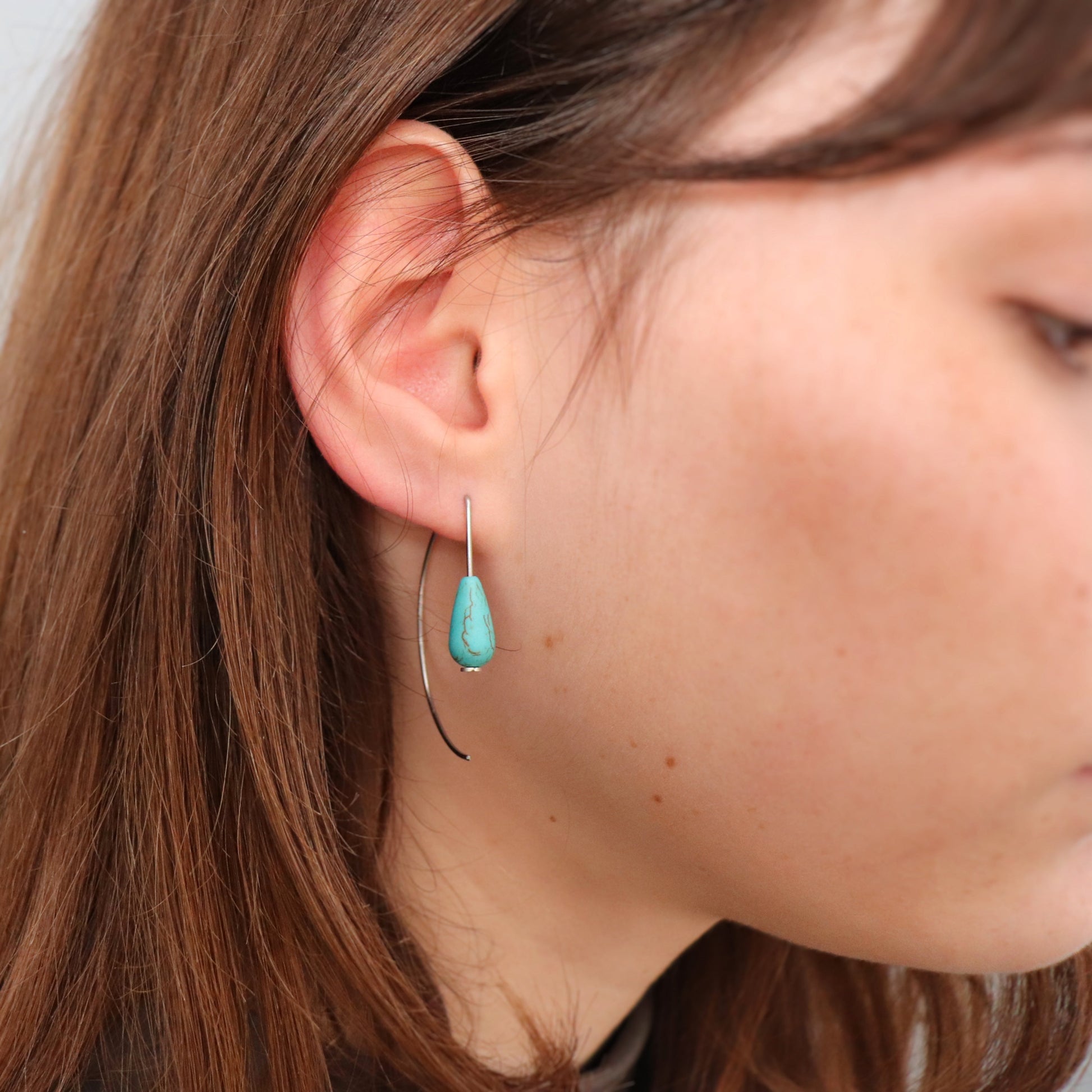 Close-up of a person wearing a turquoise teardrop earring.
