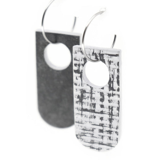 reversible earrings, one side dark grey and the other white with a grey brushed over texture, on hoops.