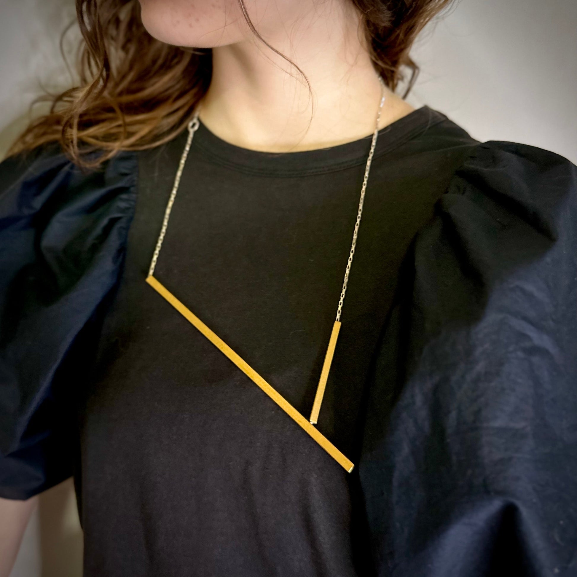Person wearing a black top with a gold geometric necklace against a neutral background