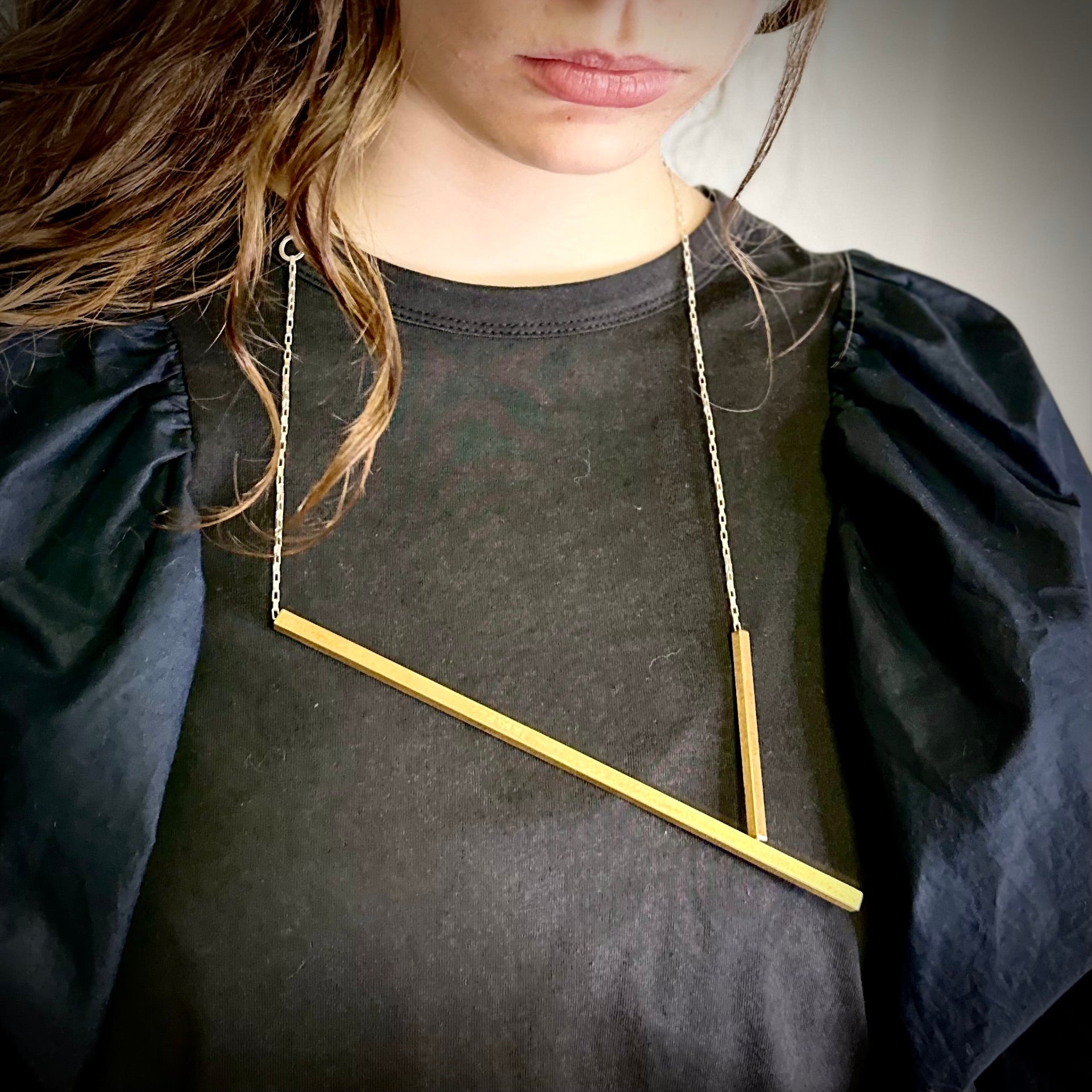 Person wearing a necklace with a gold bar pendant on a plain background