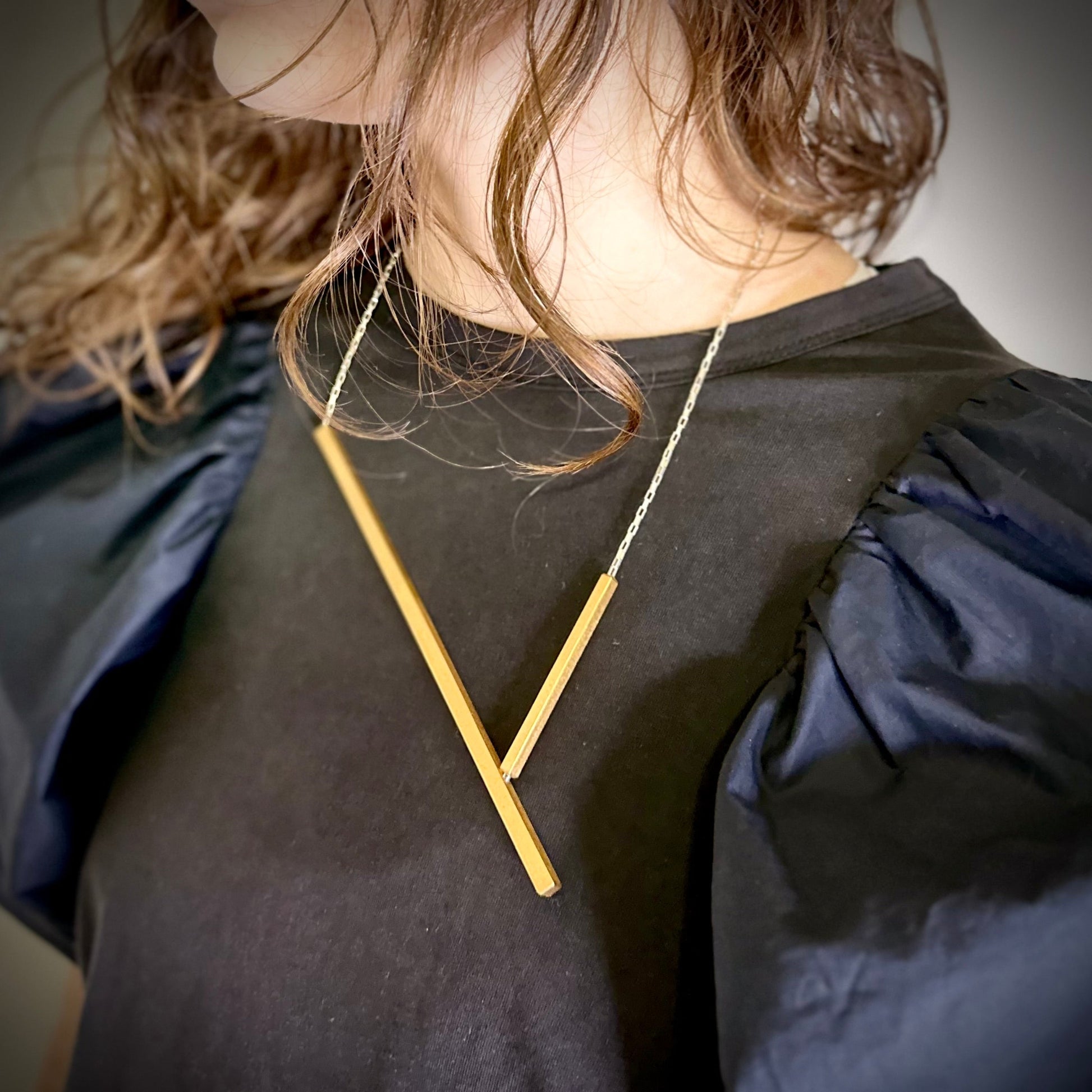 Person wearing a gold necklace with a geometric design on a dark background