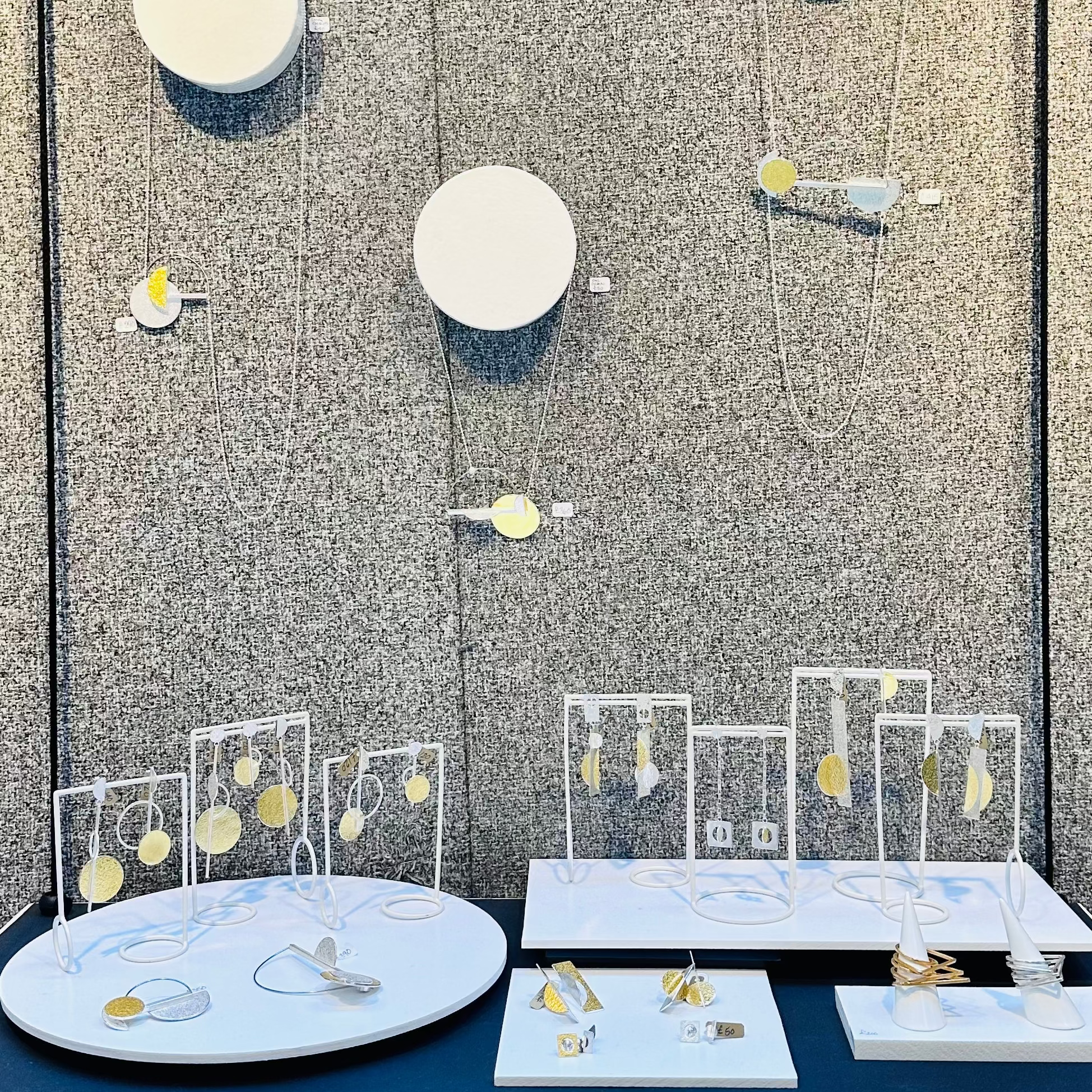 Jewelry display with various items on a table against a textured wall.