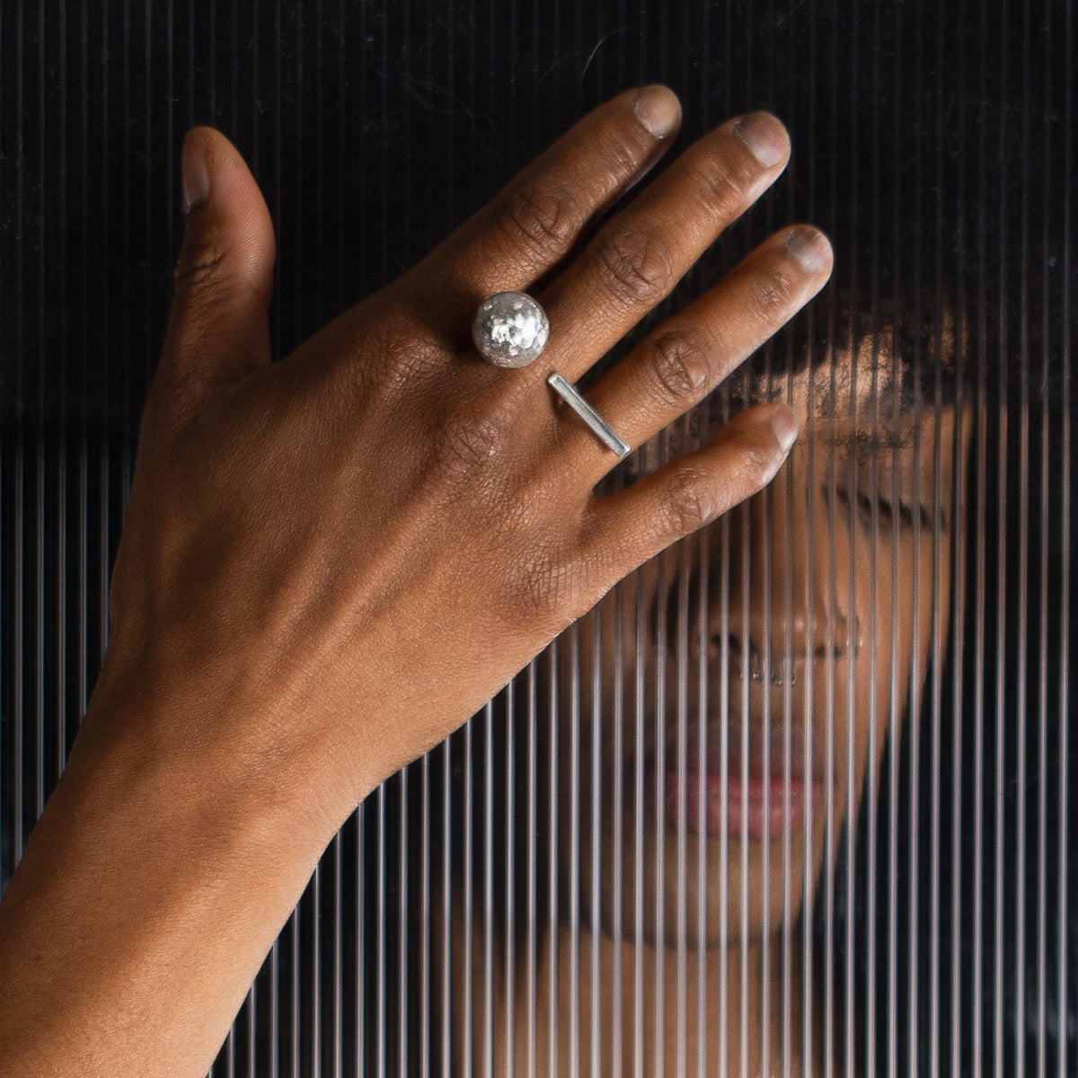 A person wearing a silver statement ring with a large ball and bar element, each on one end of the open  ring band making it appear like 2 rings.
