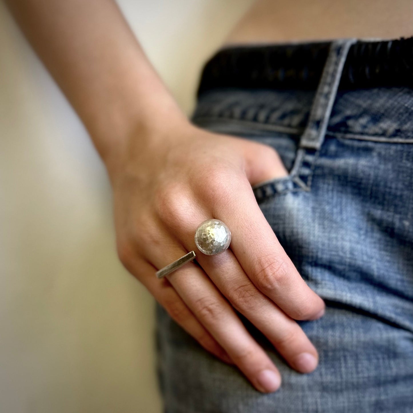 silver statement ring with a textured ball design, against a blurred background.
