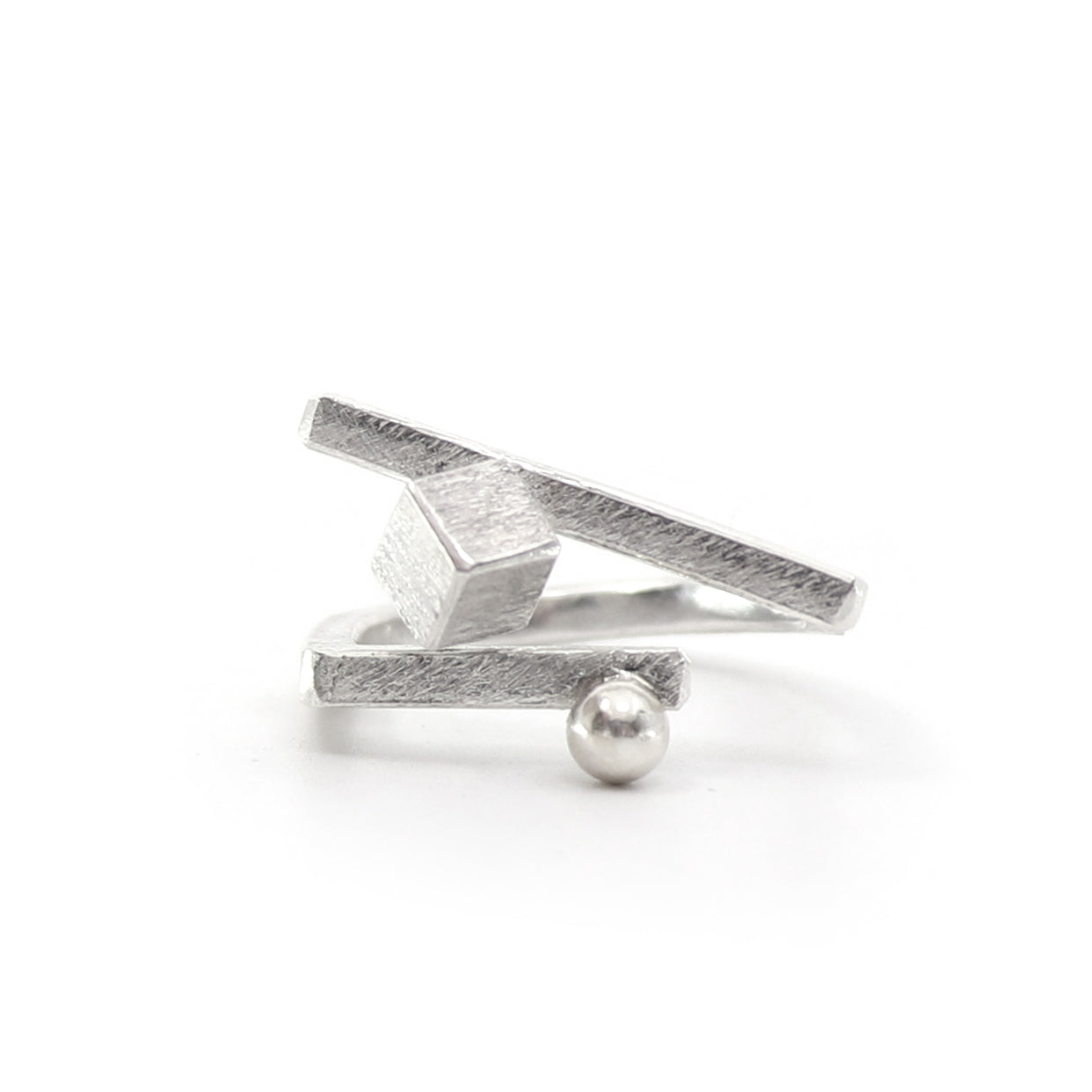A silver geometric ring featuring a textured cube and angular bars, with a small polished silver bead accent, shown on a plain white background.