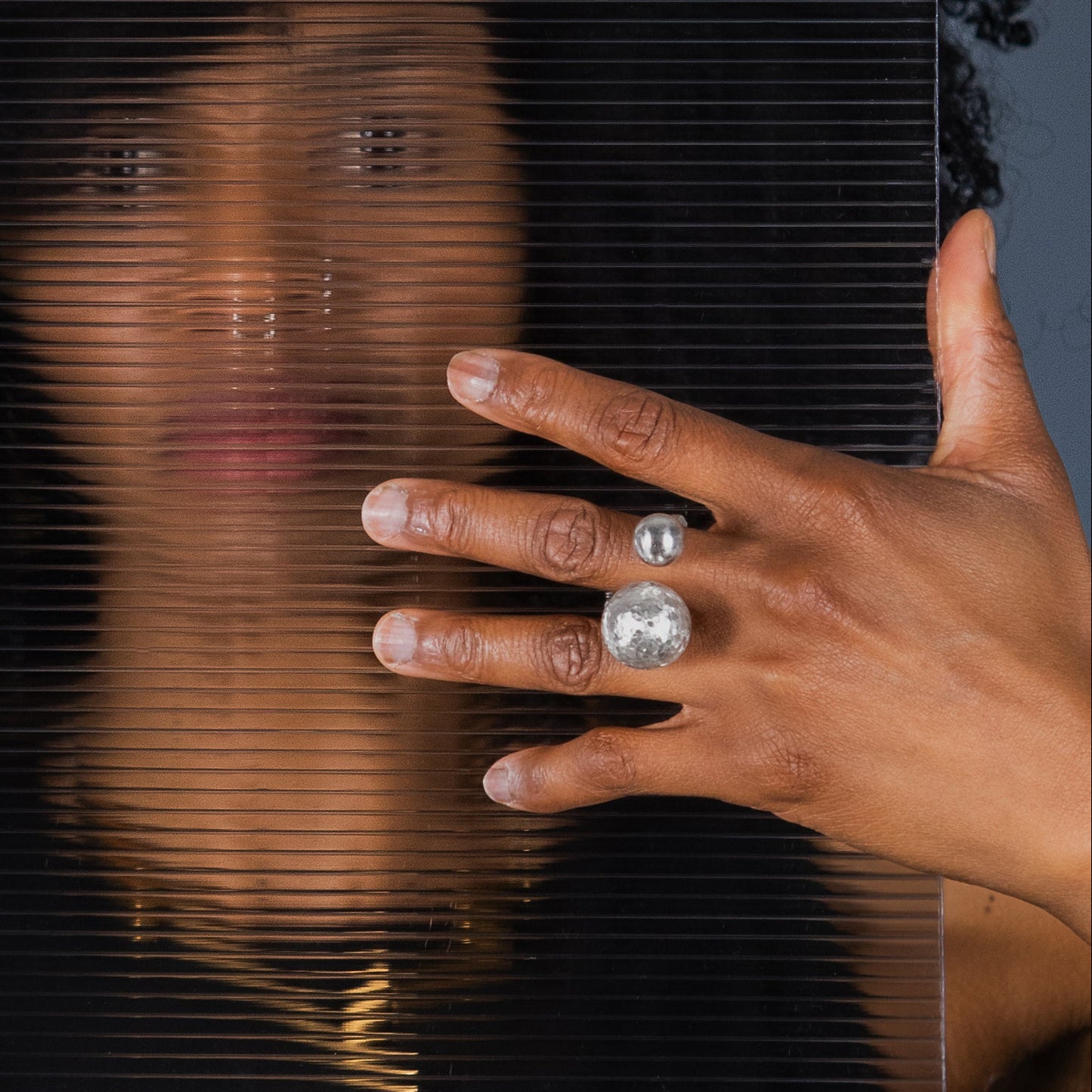 A person with dark curly modelling a statement cocktail ring made of 2 large ball elements in sterling silver. 