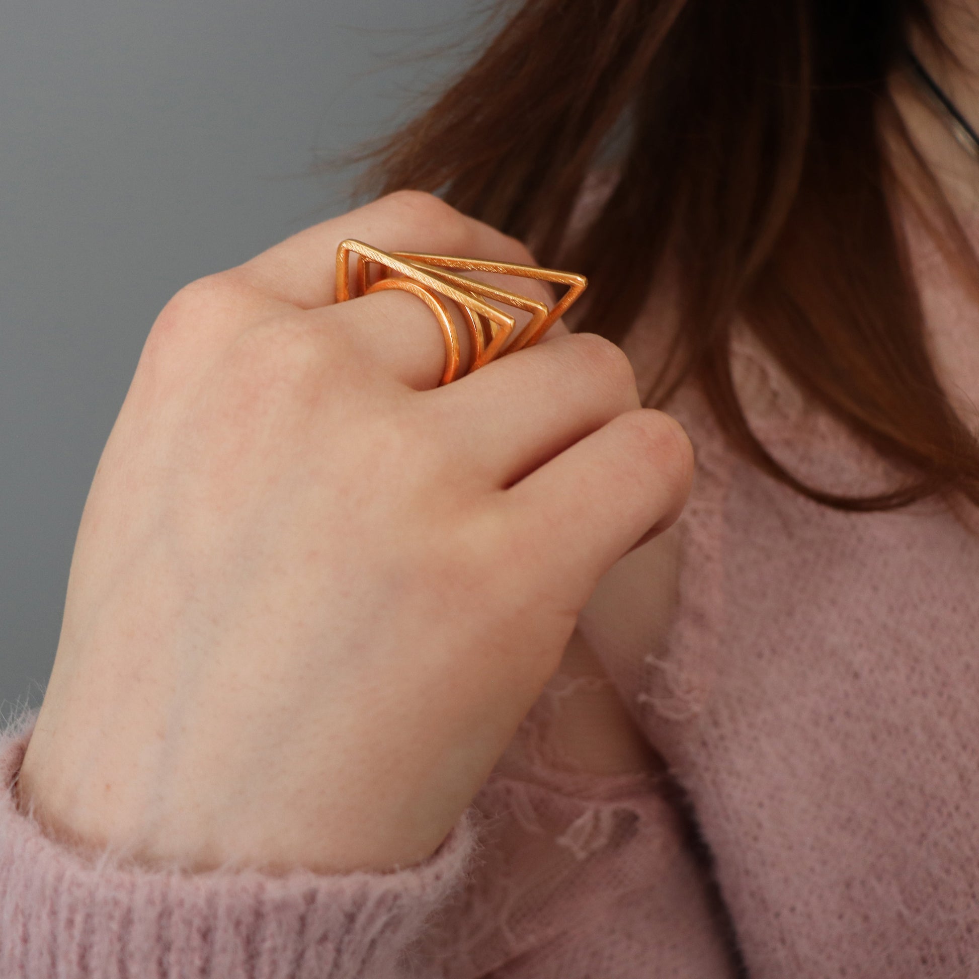 Hand wearing a geometric gold ring against a neutral background