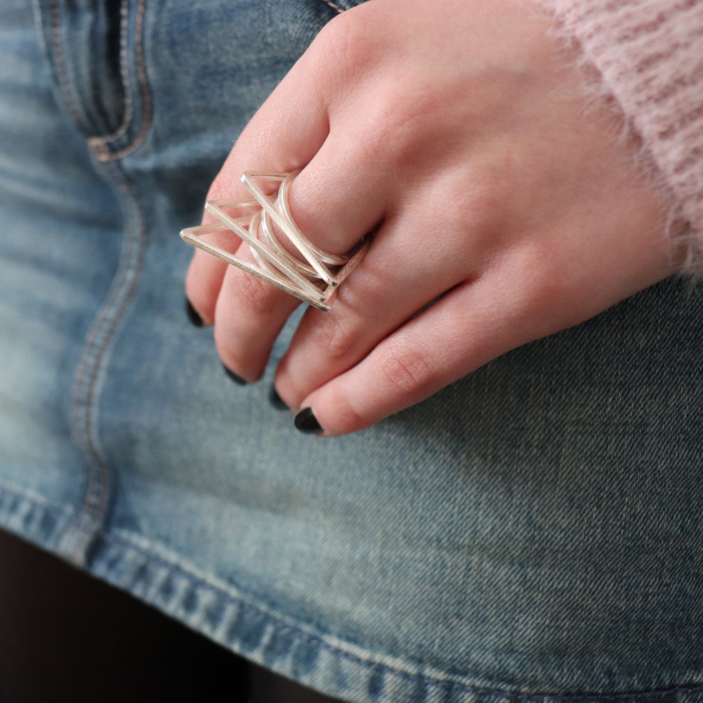 Hand wearing a silver ring with a blurred denim background