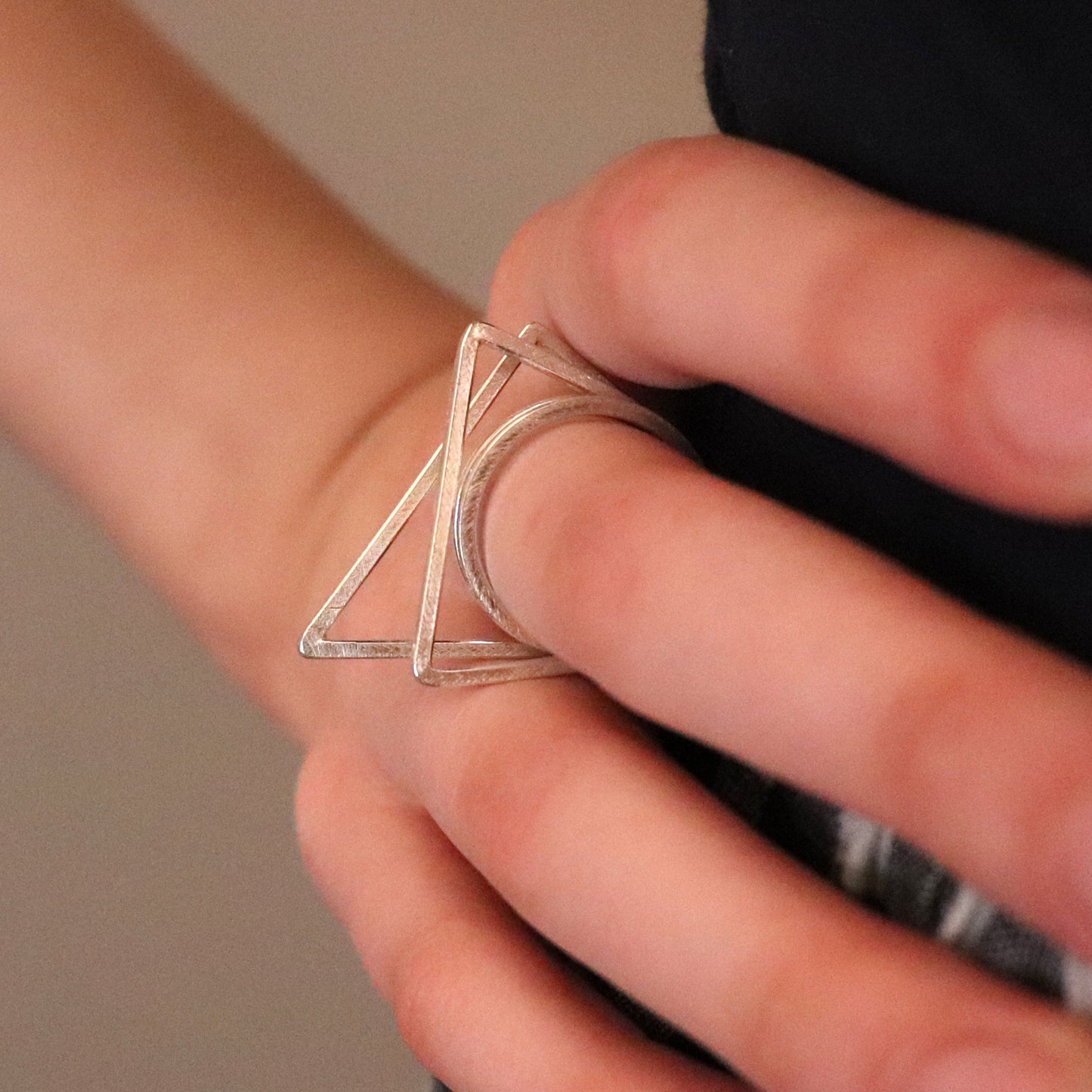 Silver triangle ring on a person's finger against a neutral background