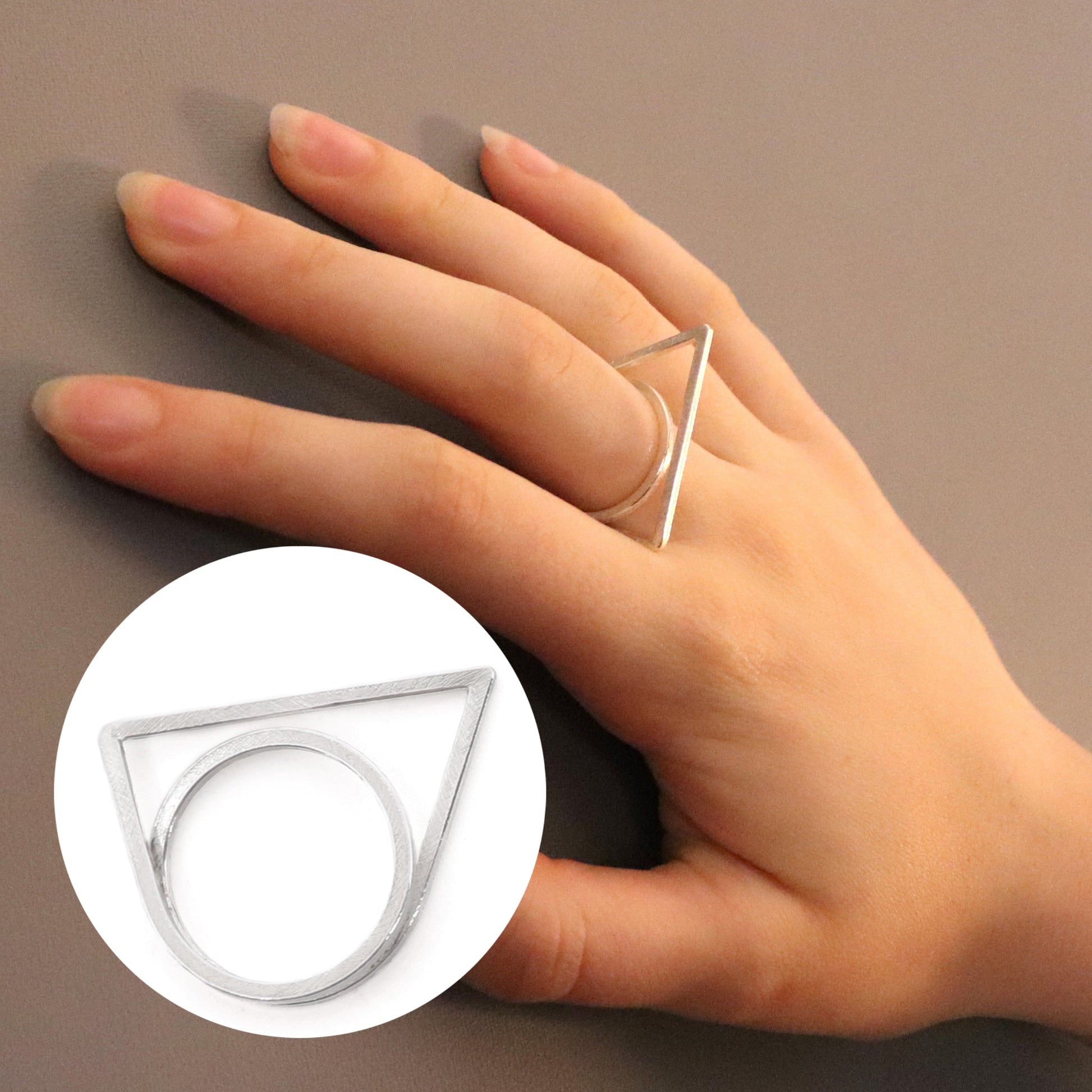 Hand wearing a silver ring with a geometric design on a neutral background