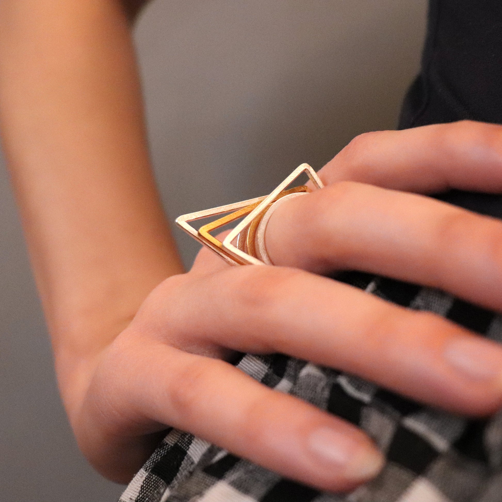 Close-up of a hand wearing a gold and silver geometric ring on a neutral background